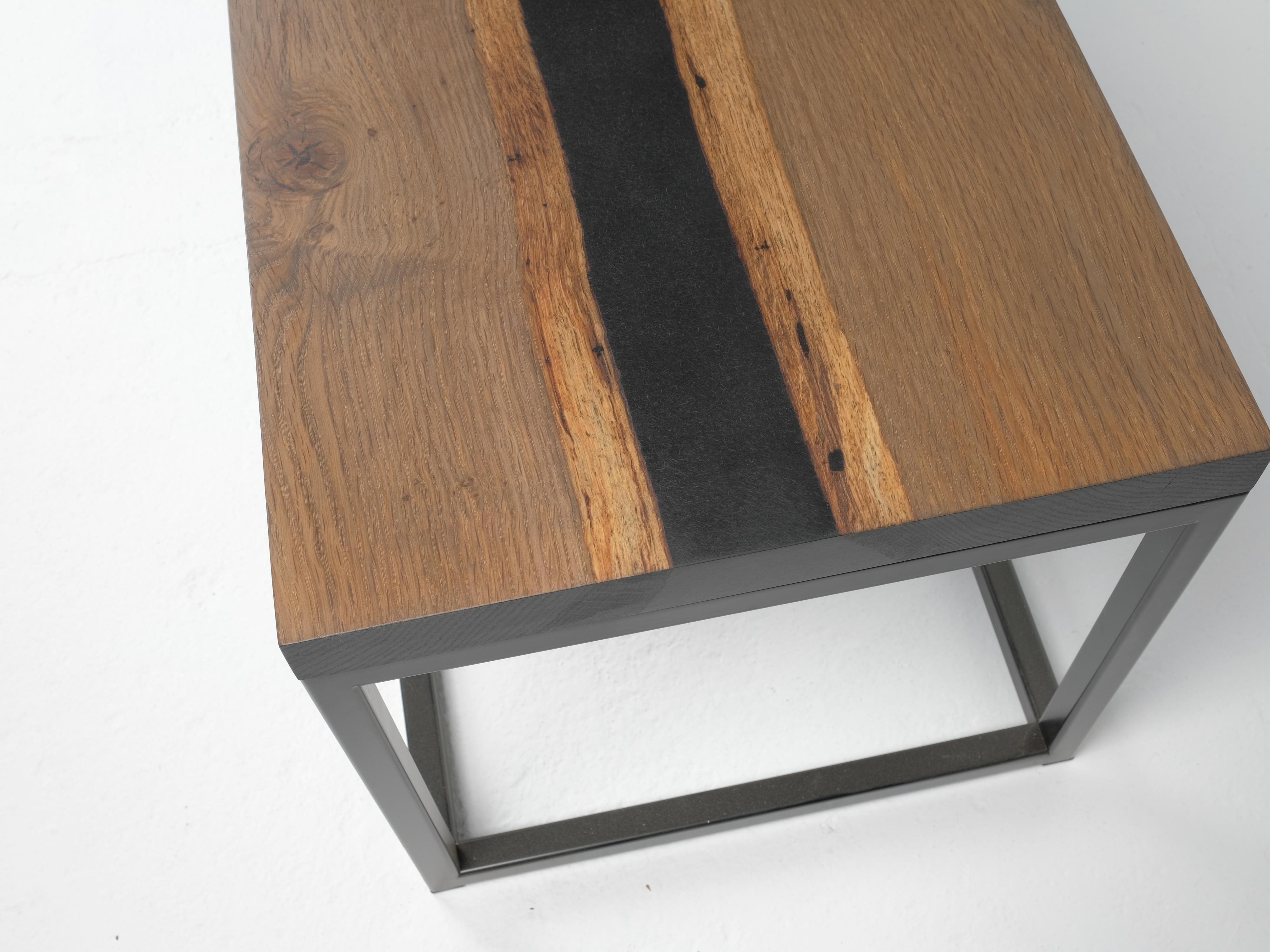This one of a kind coffee table is made from live edge white oak; fumed to bring out the tannin rich grain and features a black epoxy river. The edges are dyed black with India ink. We cut and welded the base from steel tube and powder coated it in