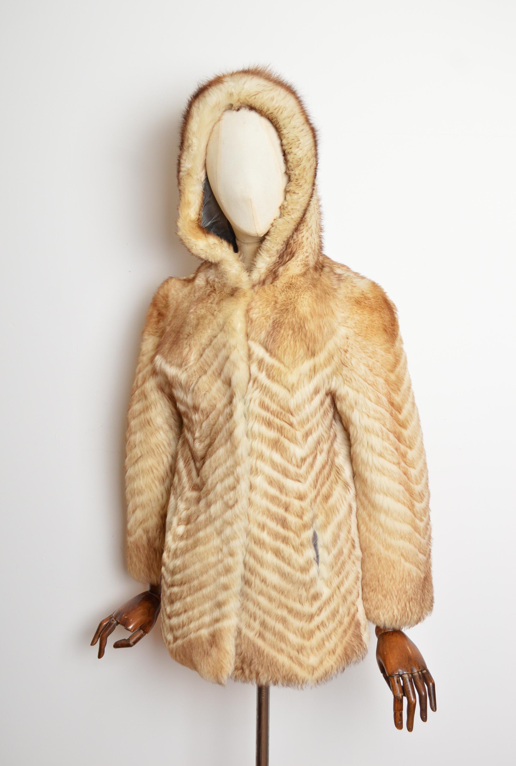 Un divertente cappotto di pelle di pecora con cappuccio degli anni '60. 
Questo caldo cappotto Lovely è caratterizzato da un design chevron, tasche sui fianchi e chiusura con gancio centrale del maniscalco. La giacca è foderata in acetato di rayon