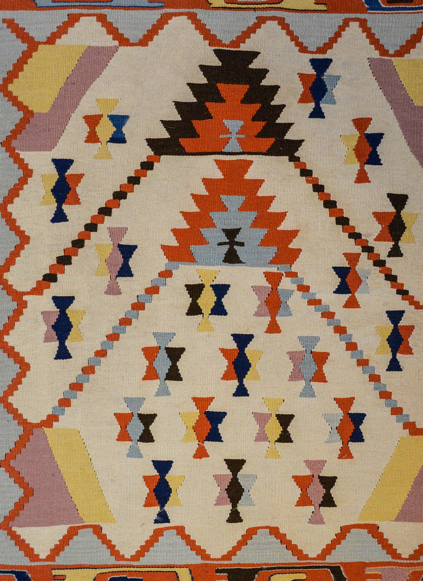 A fun vintage Indian Dhurrie Kilim rug with a bold geometric pattern woven in light and dark indigo, crimson gold, black and white wool surrounded by a pale indigo and crimson zigzag patterned border.