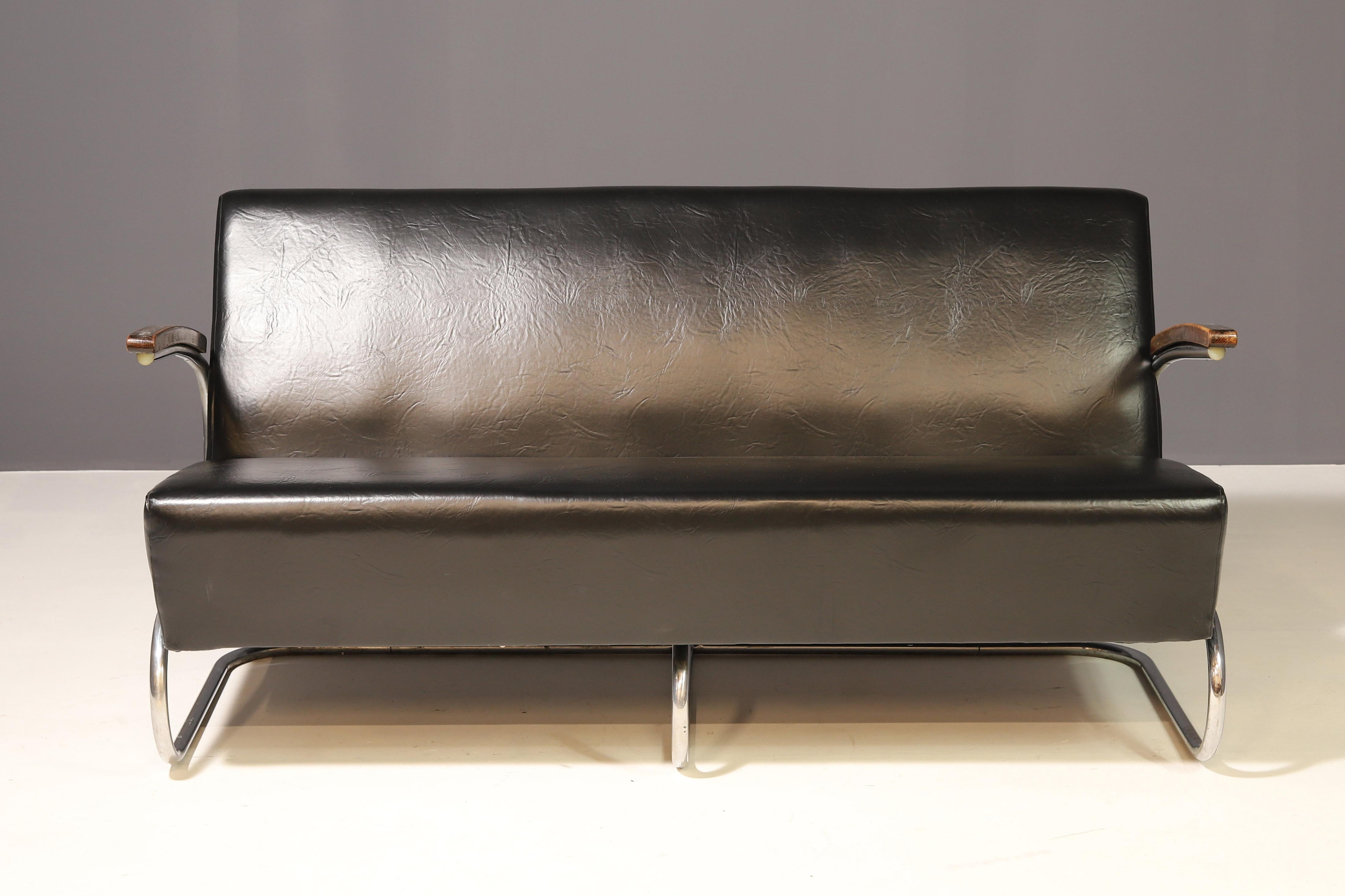 Este sofá funcionalista fue fabricado por Kovona (antes Hynek Gottwald, Brandýs nad Orlicí) y sigue el diseño original de Marcel Breuer, adaptado posteriormente por Antonín Lorenc para Thonet. Presenta un armazón de tubo de acero cromado,
