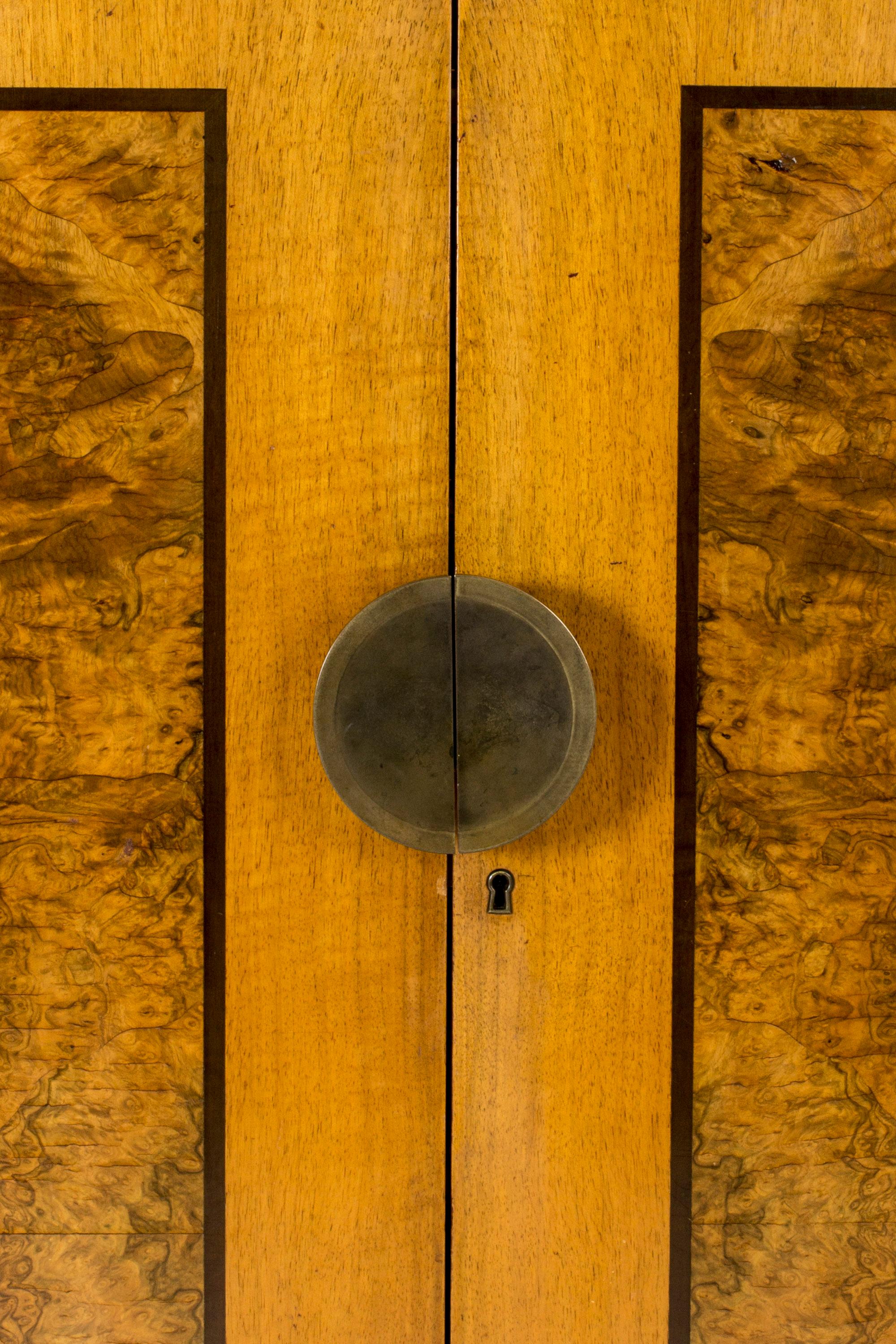 Stately functionalist cabinet by Erik Chambert, made from birch with birch root inlays. Large round brass door handle that splits seamlessly when the cabinet is opened. Elegant inside made from darker wood with contrasting drawer handles. A mirror