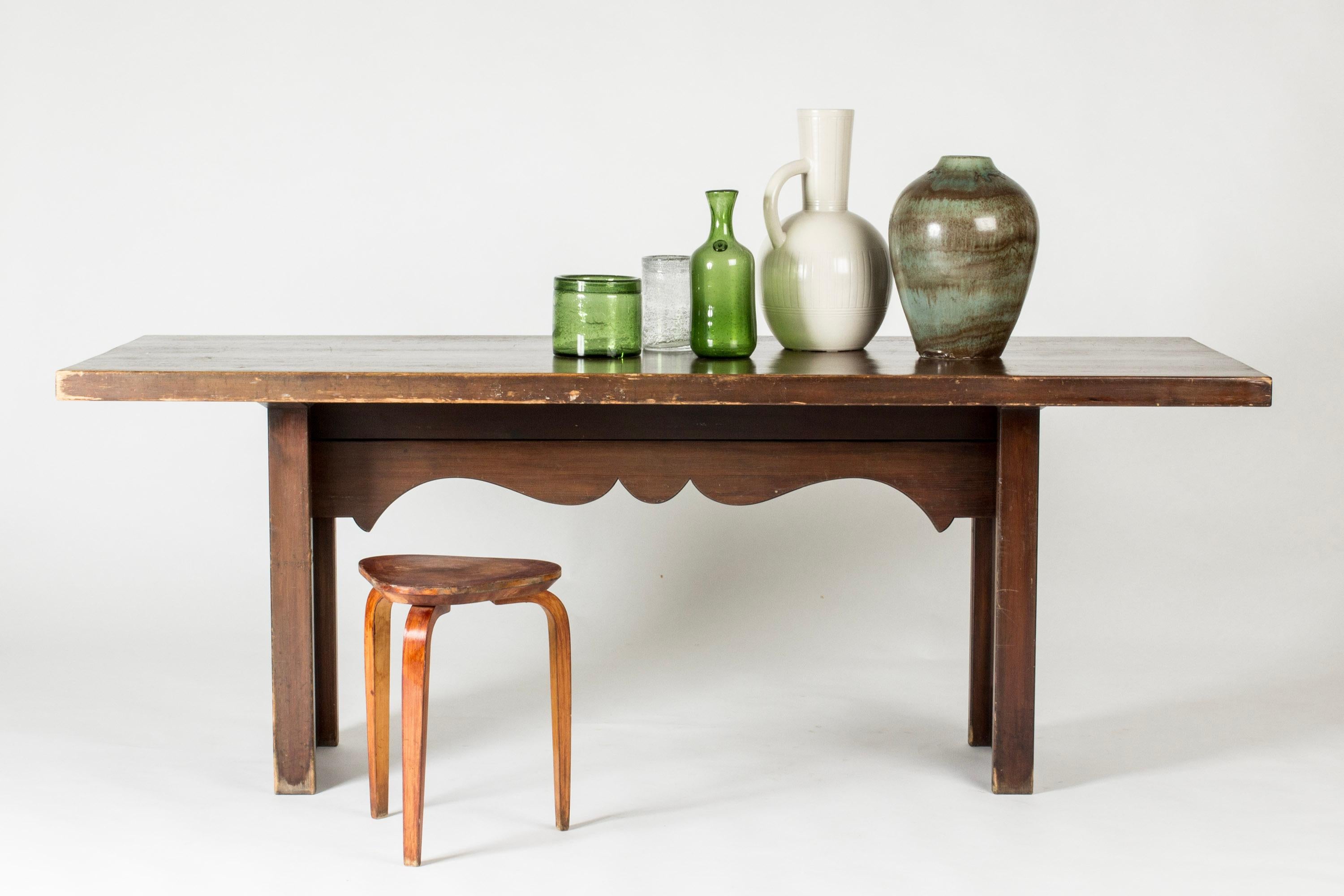 Table de salle à manger de Carl Malmsten, au design rustique. Fabriquée en pin teinté, elle présente des lignes épurées et un détail décoratif folklorique sous le plateau de la table.