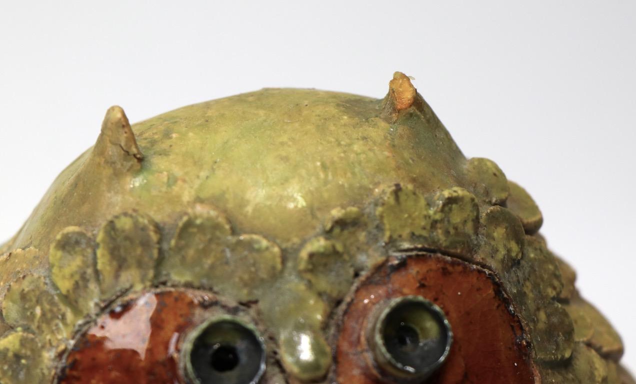 Very funky pottery owl with enameled metal eye sockets. This piece dos have some condition issues, notably one ear is repaired, one is missing, and there is some loss to the ceramic feathers, as shown, signed illegibly. Althoughtnot in perfect