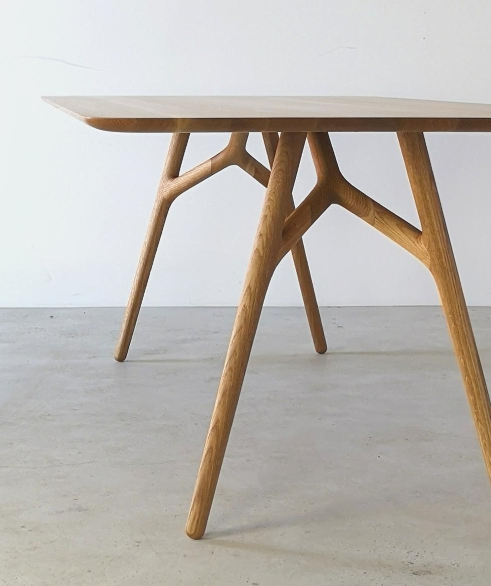 La Furcula d'Izm Design est une table de salle à manger élégamment fabriquée à la main, dotée d'un pied sculpté en forme d'arête et d'une large gorge composée sur la partie inférieure du plateau. S'intègre parfaitement aux designs modernes,