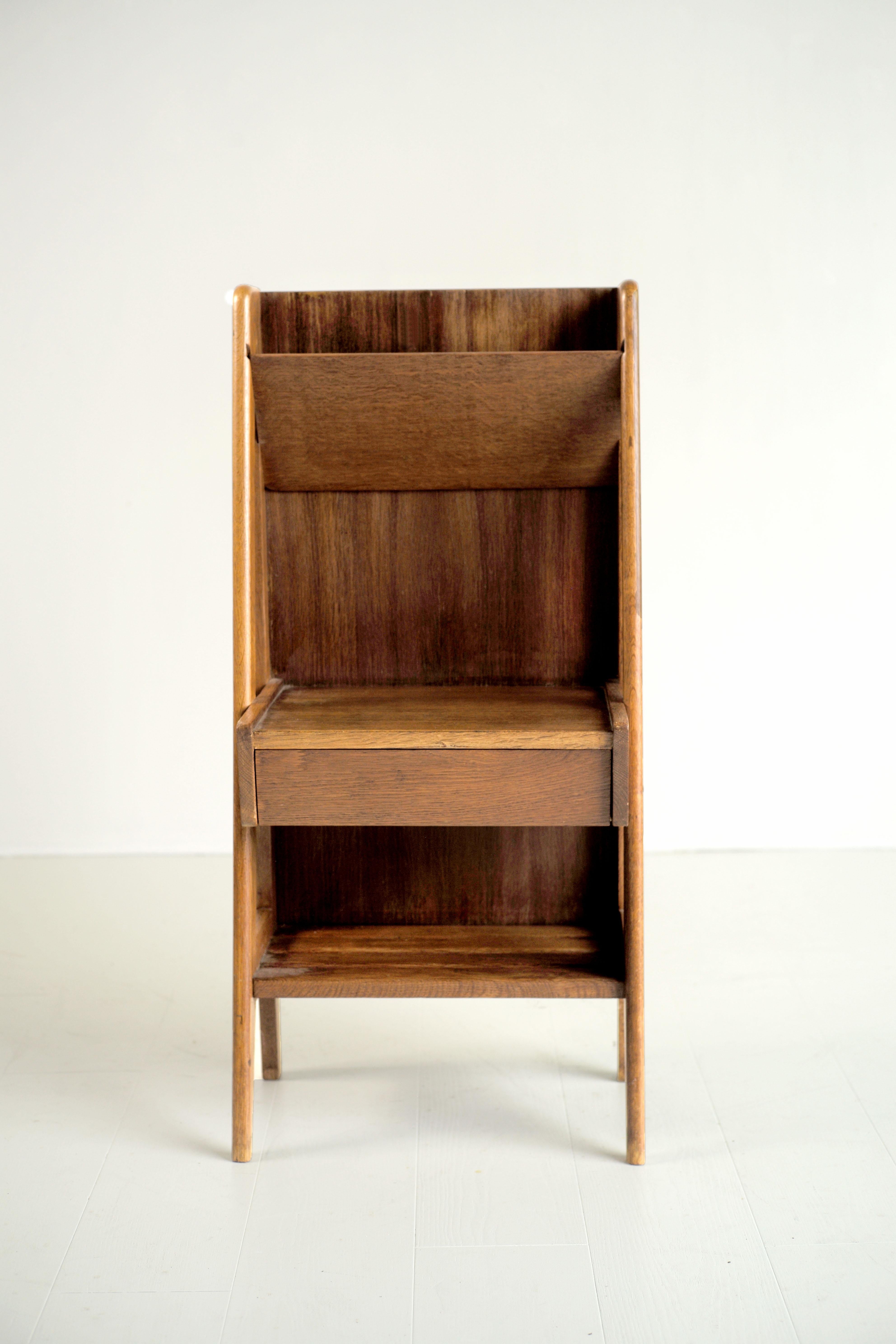 Occasional oak furniture dating from the French Reconstruction, 1950. On a compass base is positioned a drawer unit, topped with a newspaper compartment. At the base is a slatted shelf. As interesting in its design as in its ingenuity, this piece of