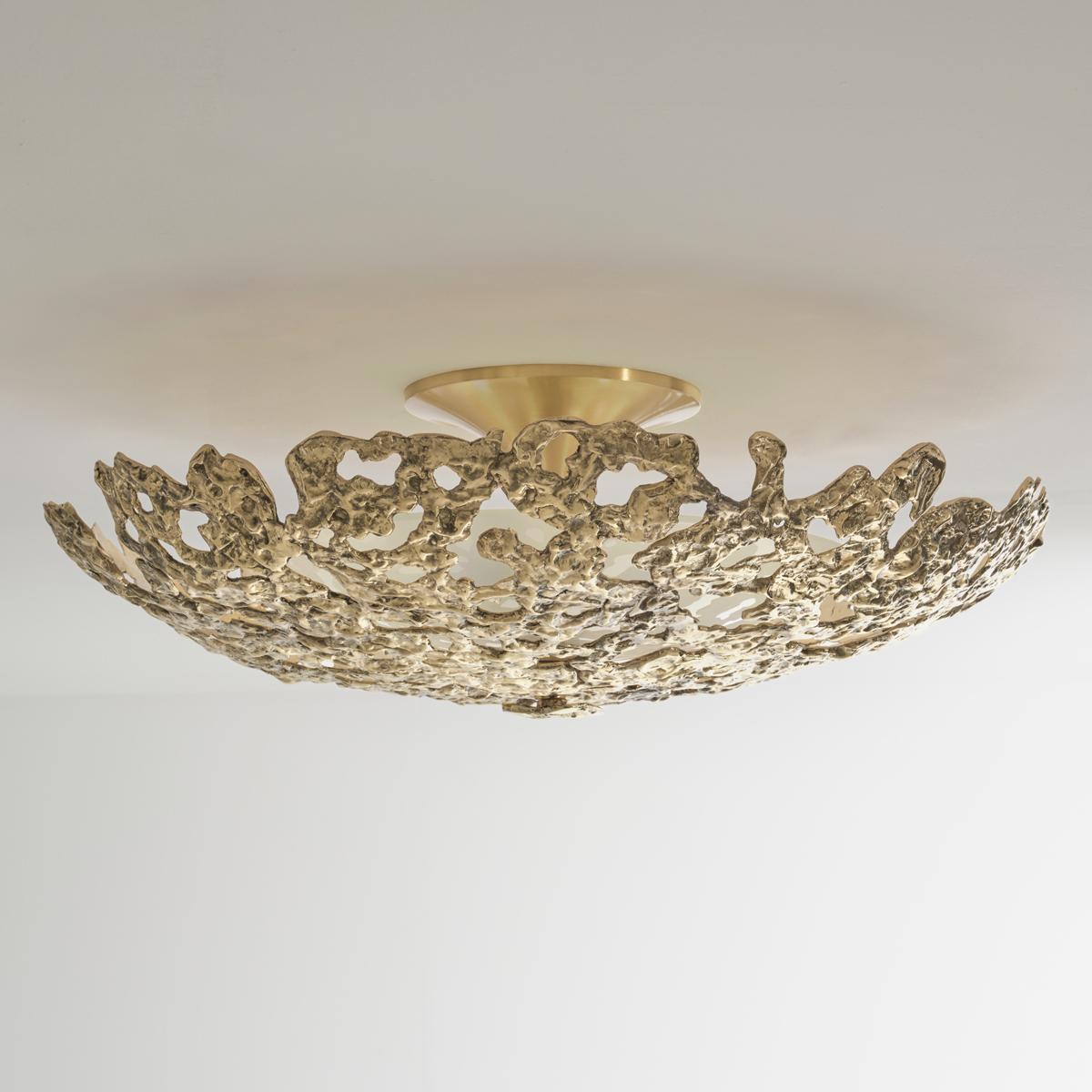 The Fusione Grande ceiling light features a sculptural cast brass shade characterized by amorphous edges and perforations. Internally it holds a frosted glass diffuser concealing the light sources. The sleek conical canopy creates a natural contrast