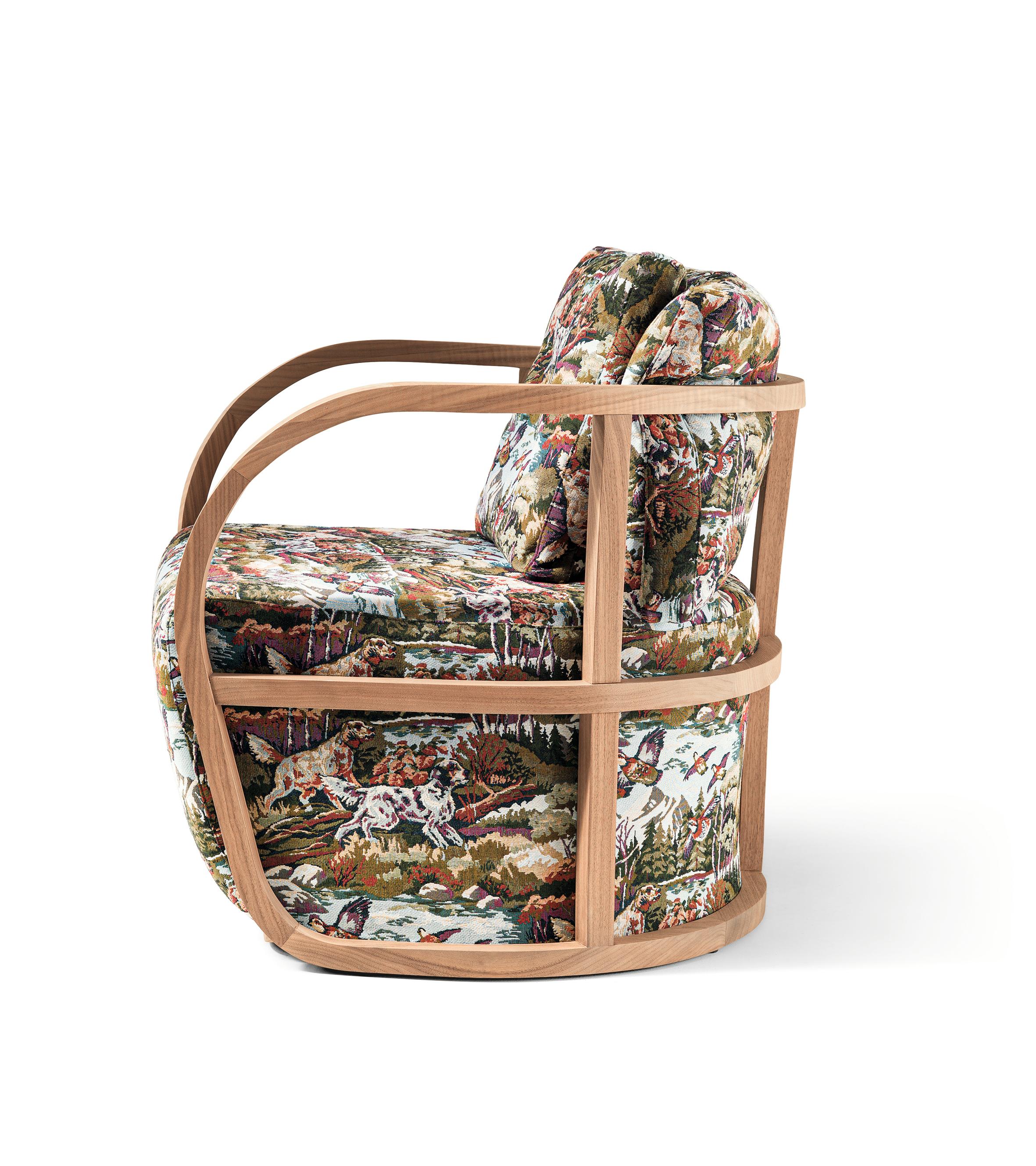 Sillón de salón tapizado con armazón curvo visible de nogal Canaletto macizo mate. La tela representa una escena de caza con perros. Está disponible en todos los tejidos de las colecciones y también en COM.