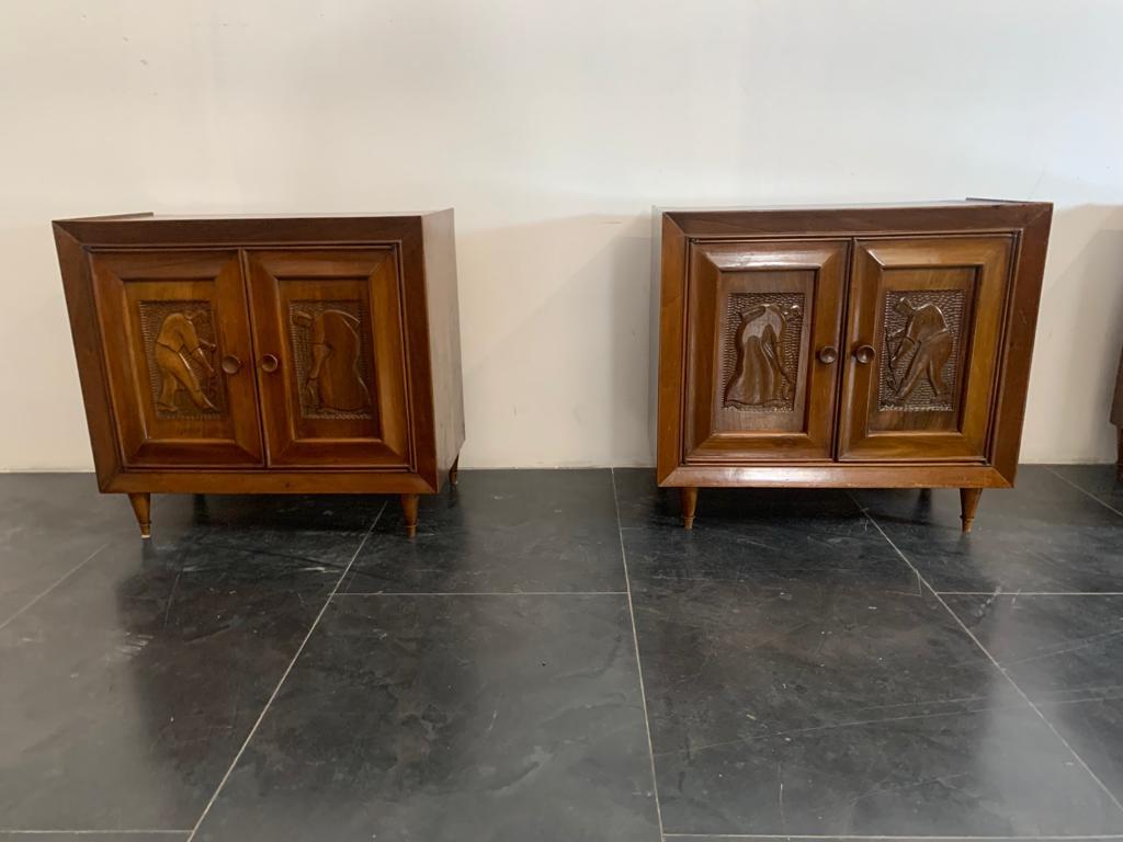 Bedside tables of great quality in solid walnut, have door with carved panels with characters of futurist taste on gouged background. They rest on conical feet with brass ferrules. The lines are typical of the 50's but clues in the manufacture and