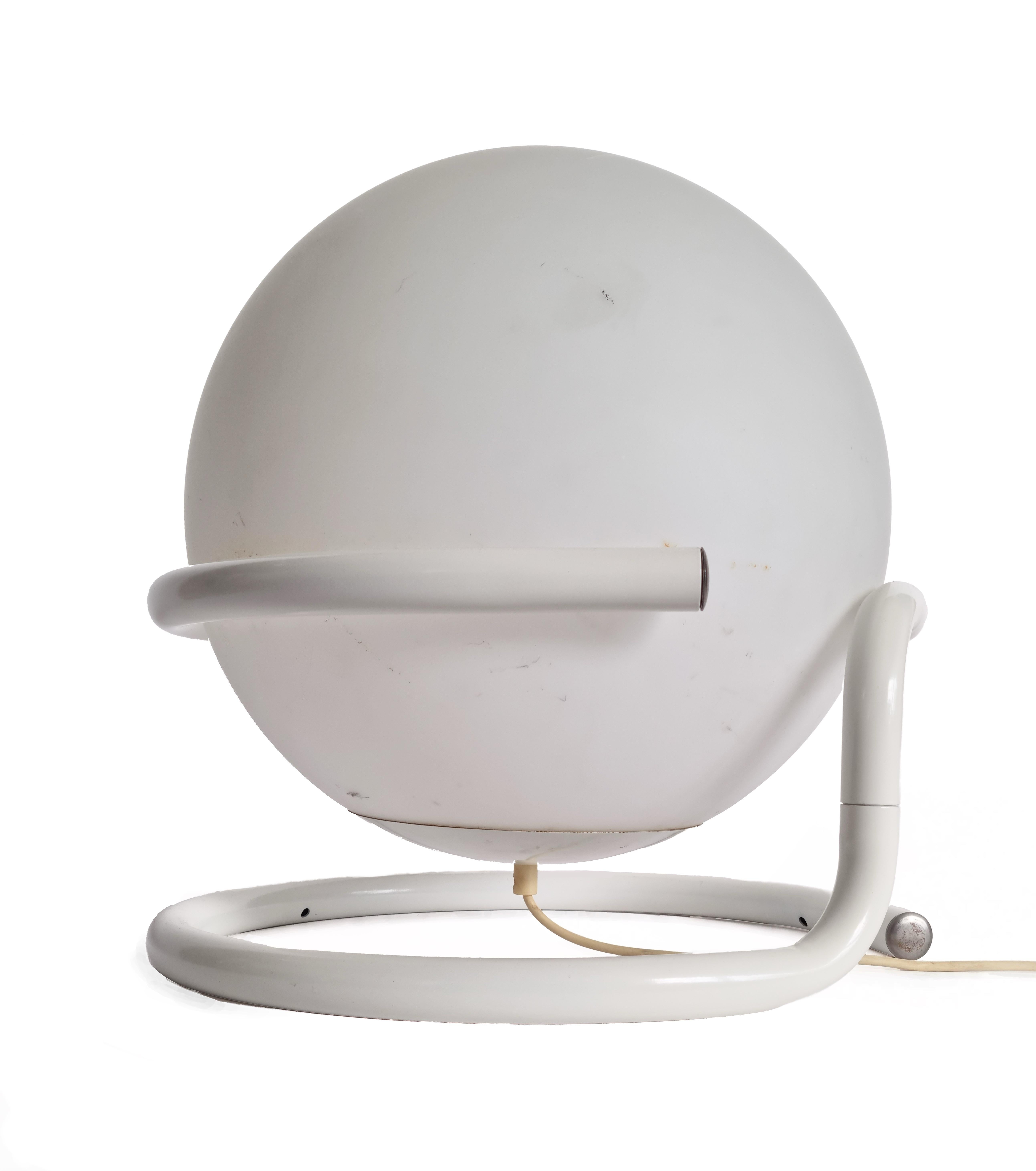 This iconic vintage table lamp from the 1970s is a striking example of space age design. Featuring a bold, spherical shape nestled within a circular metal frame, the lamp evokes the look of a retro-futuristic planet or space capsule. Crafted in