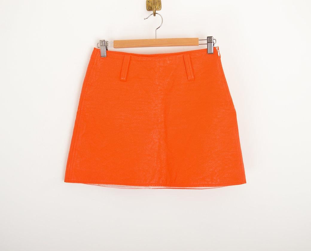 Iconic and Futuristic orange vinyl mini skirt by Courréges.
Circa 2000.
 
Features;
Conceal zip up side
Belt loops
A-Line shape
Fully lined
85% Cotton / 15% Polytheurane 
 
Sizing;
Waist; 28''
Length; 15''

The jacket is also available to purchase