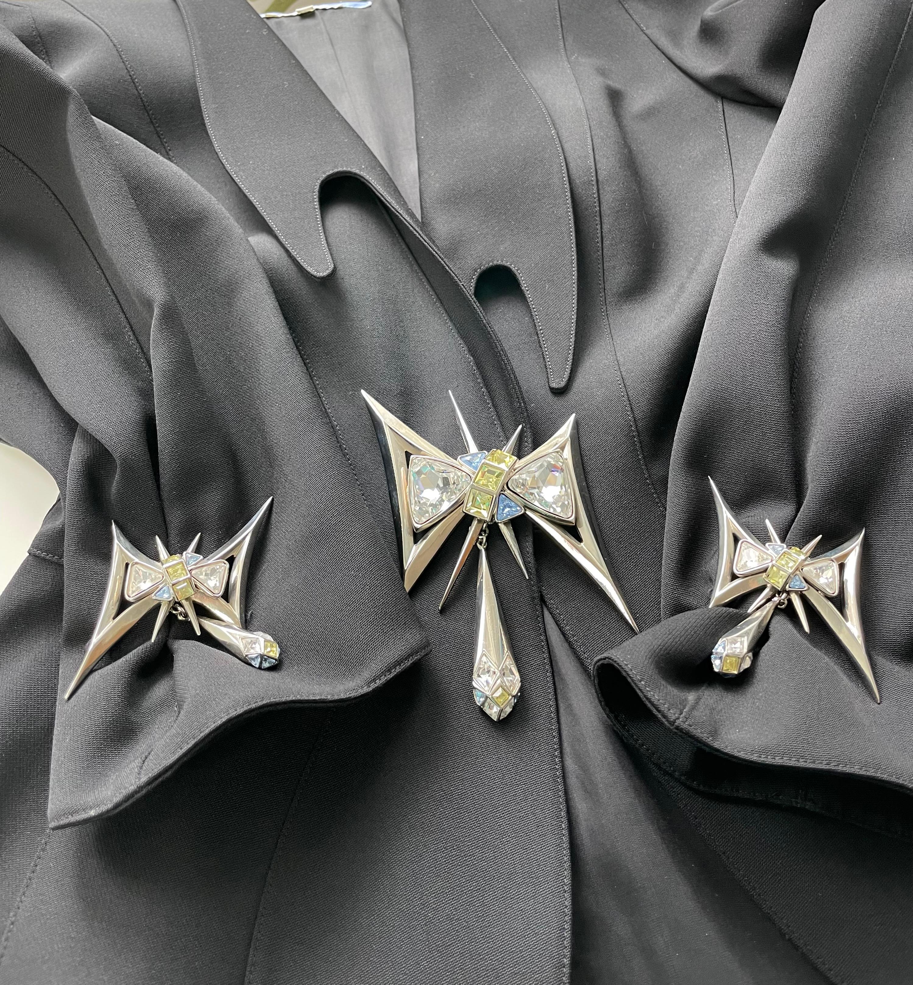Espectacular chaqueta Thierry Mugler de la colección otoño-invierno 1994 Quaker Splash. Adornada con grandes broches de strass incrustados en el cierre delantero y en los puños. Bonita solapa asimétrica con bordes afilados. Cierre con botones de