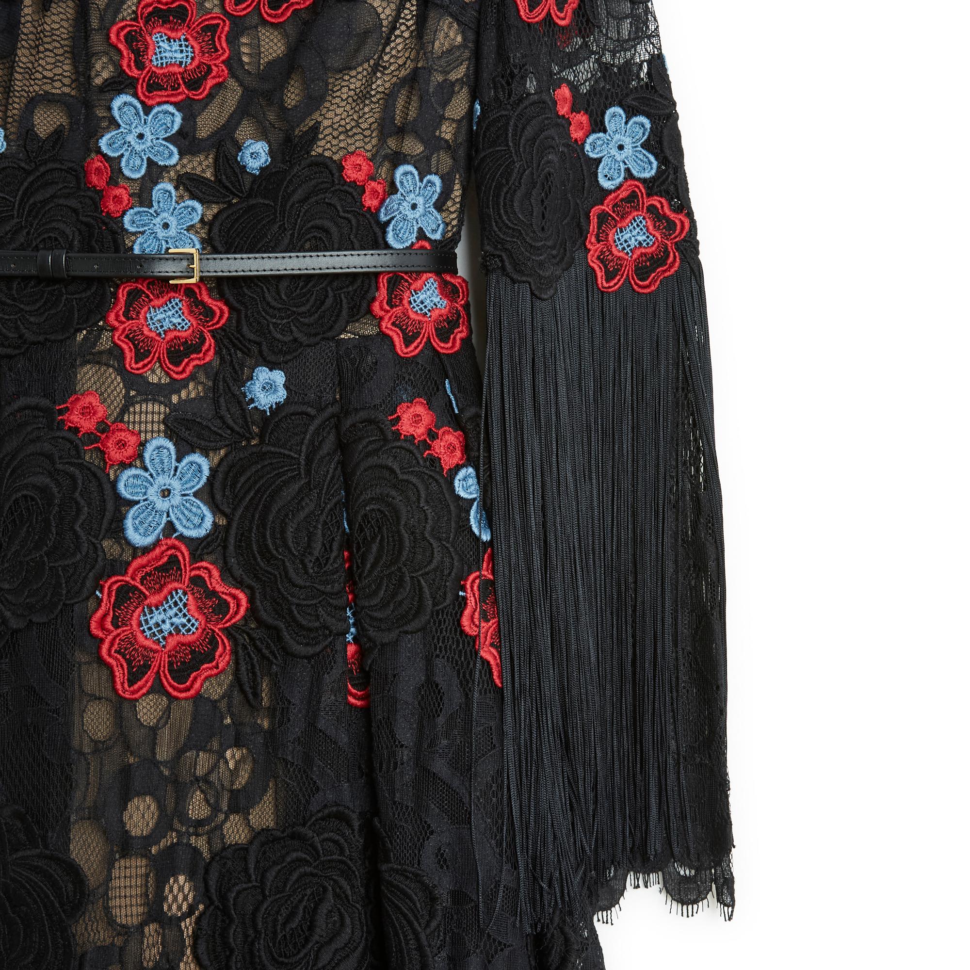 Elie Saab short dress AW2016 collection in black lace embroidered with red and blue flowers, round neck, long sleeves lined with fringe from the elbow, thin leather belt at the waist, skirt with large box pleats, flesh-colored silk crepe lining on