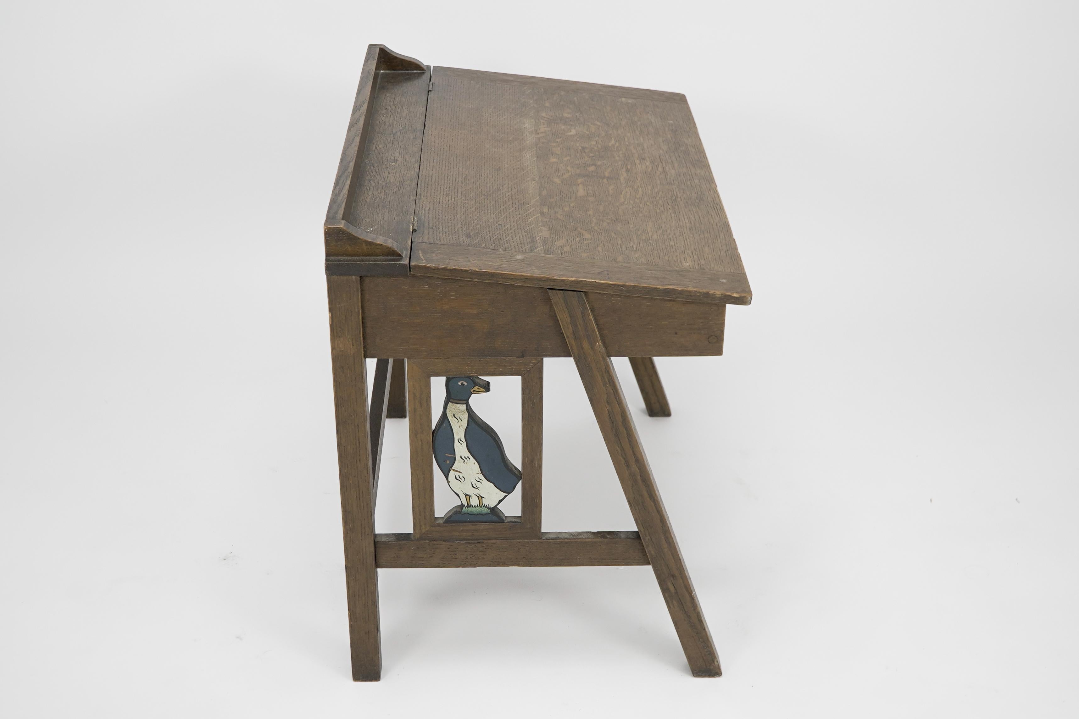 G F Hardy Manchester. Bureau d'enfant en chêne de style Arts and Crafts, avec un espace d'écriture incliné et un espace de rangement en dessous. Les côtés sont sculptés et peints en polychromie avec un gentil petit lapin et un canard dans un cadre.