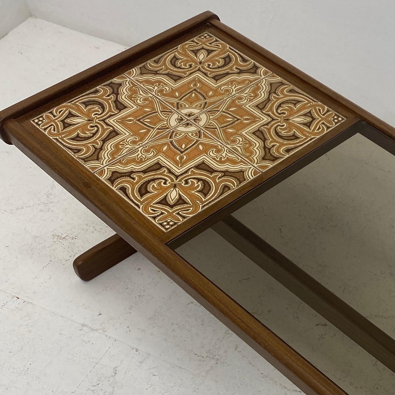 A 1960s rectangular long coffee table by G Plan designed by Victor Wilkins. The coffee table is part smoked glass and part ceramic tiled top on a solid teak frame. The tile is in a floral orange & brown pattern. The coffee table legs are a great