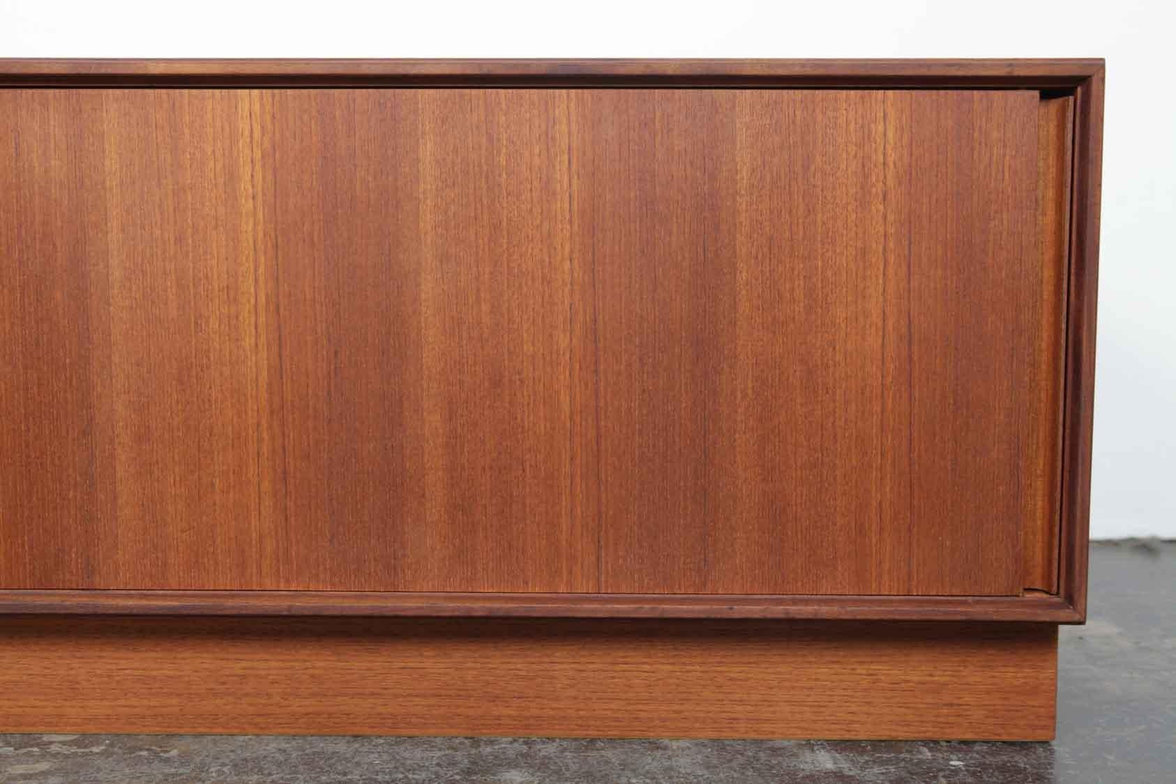 Low teak plinth based two-door sideboard by G Plan, 1960s, England. The seamless front gives way to doors that slide behind each other in a unique way. Newly refinished in a natural teak oil.