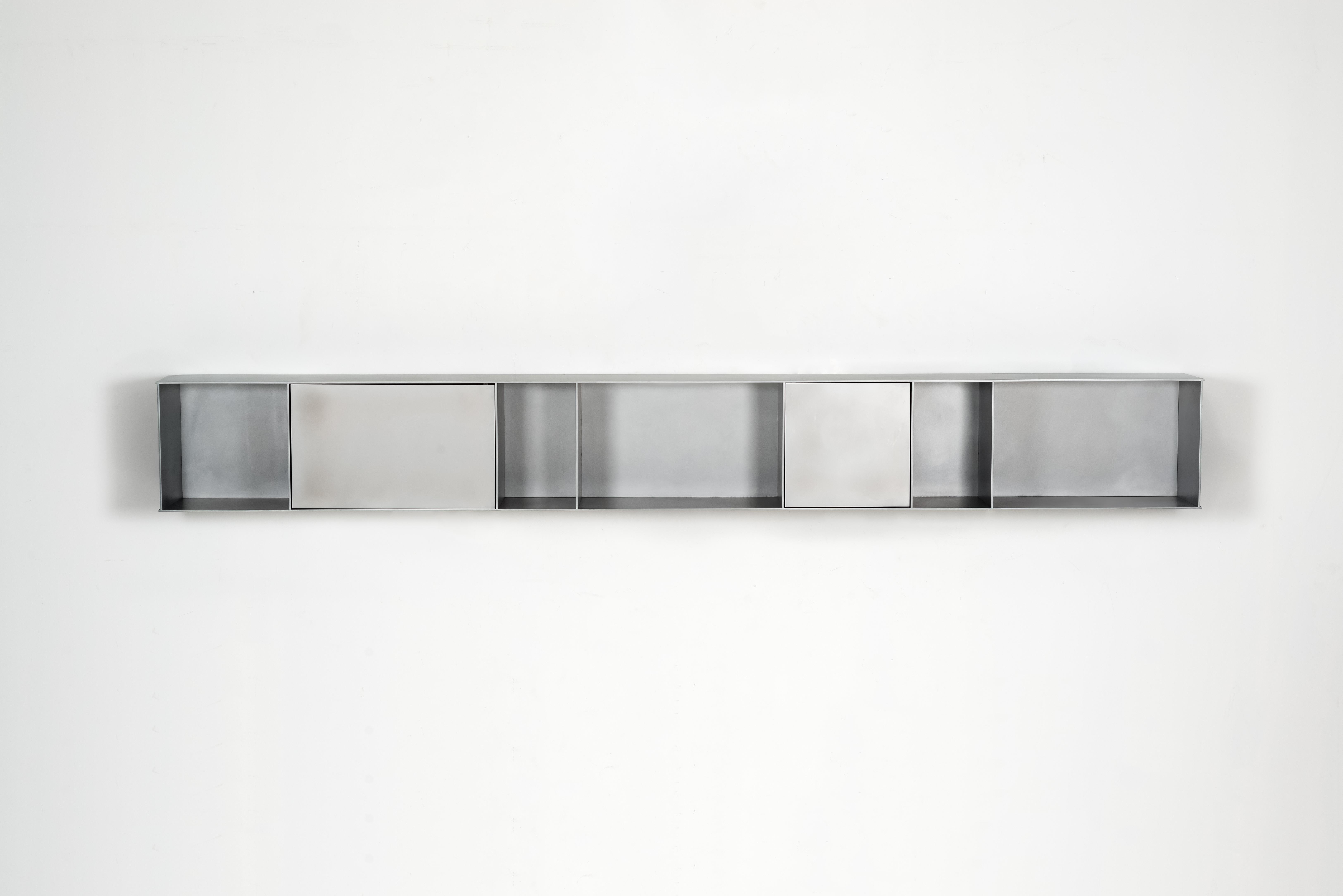 The Minimalist wall-mounted G shelf is sculpted out of 1/4 inch thick, wax-polished aluminum with three pin-hinged doors. Each shelf has an inset welded U-channel that spans the length of the shelf and easily mounts on included custom-bent steel