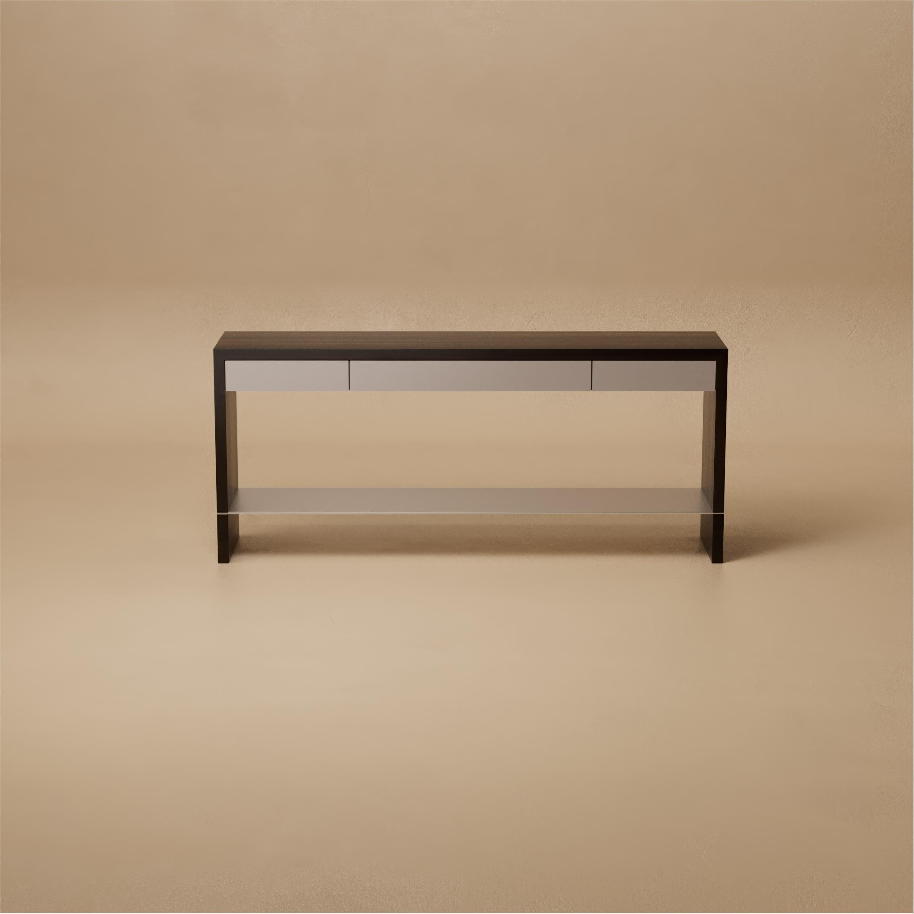 Il tavolo consolle Grant è una raffinata semplicità resa architettonica. I cassetti laccati satinati scorrono sotto una struttura in noce, mentre un sottile ripiano in metallo e i cassetti intarsiati in pelle aggiungono dettagli sottili. Ogni