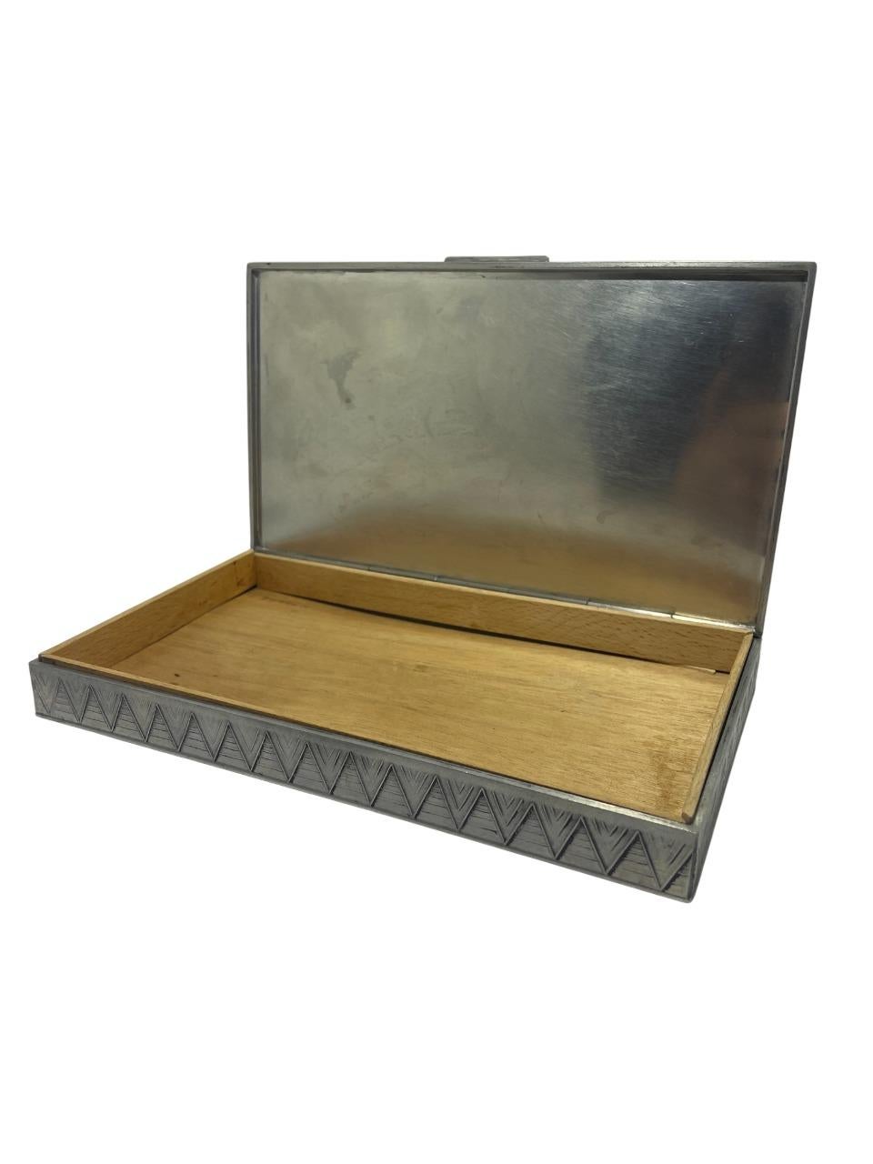 An elegant pewter lidded box crafted by GAB (Guldsmedsaktiebolaget), Sweden, dating to the 1930s. This rectangular box features a striking Art Deco zigzag pattern etched along the sides and a refined monogram “GS” engraved on the lid. The interior