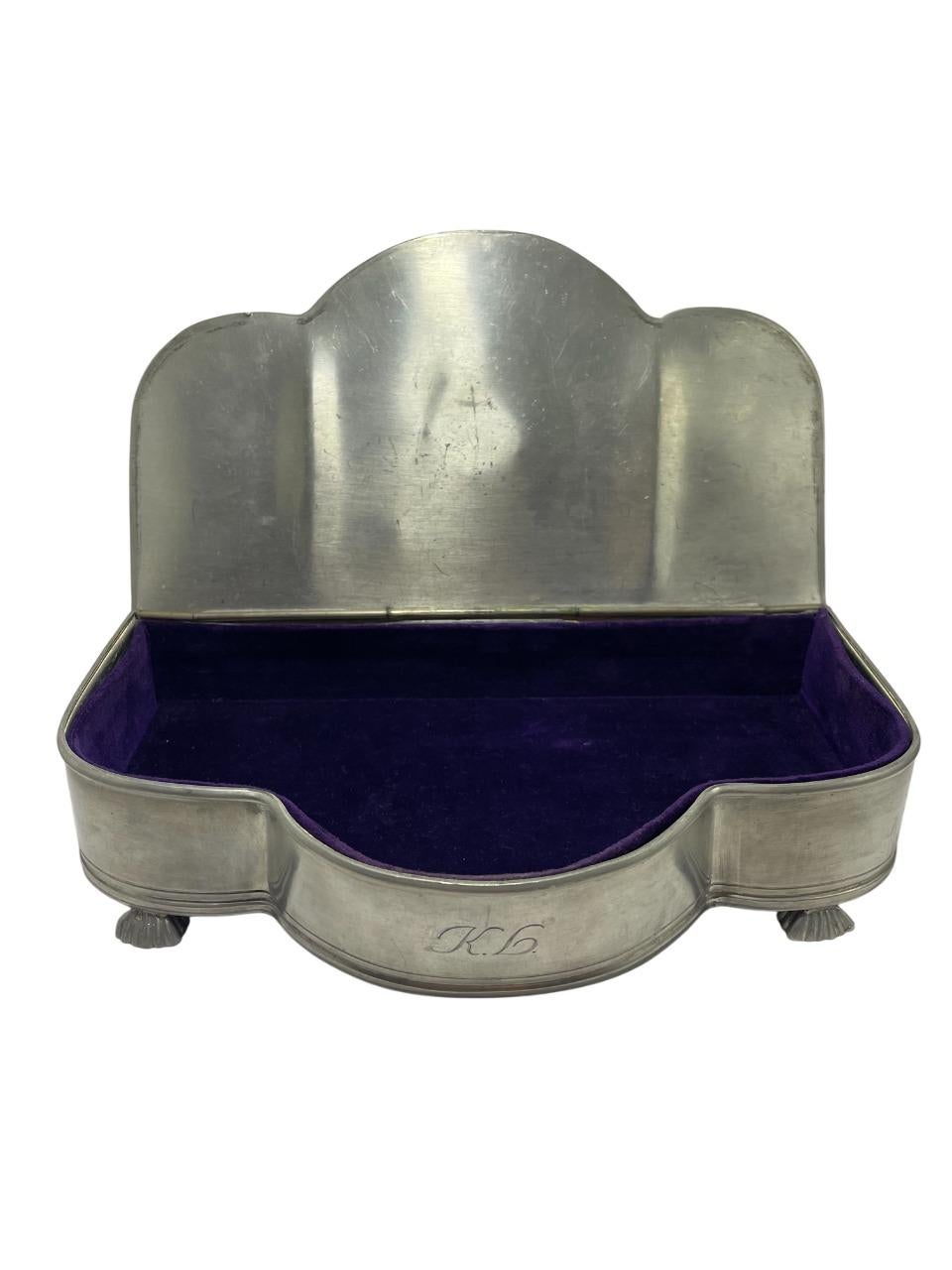 Elegante joyero sueco de estaño fabricado por Guldsmedsaktiebolaget (GAB) en la década de 1930. Esta hermosa pieza presenta la silueta de un piano de cola, apoyada sobre patas en forma de concha y adornada con un escultural remate de rosa en la