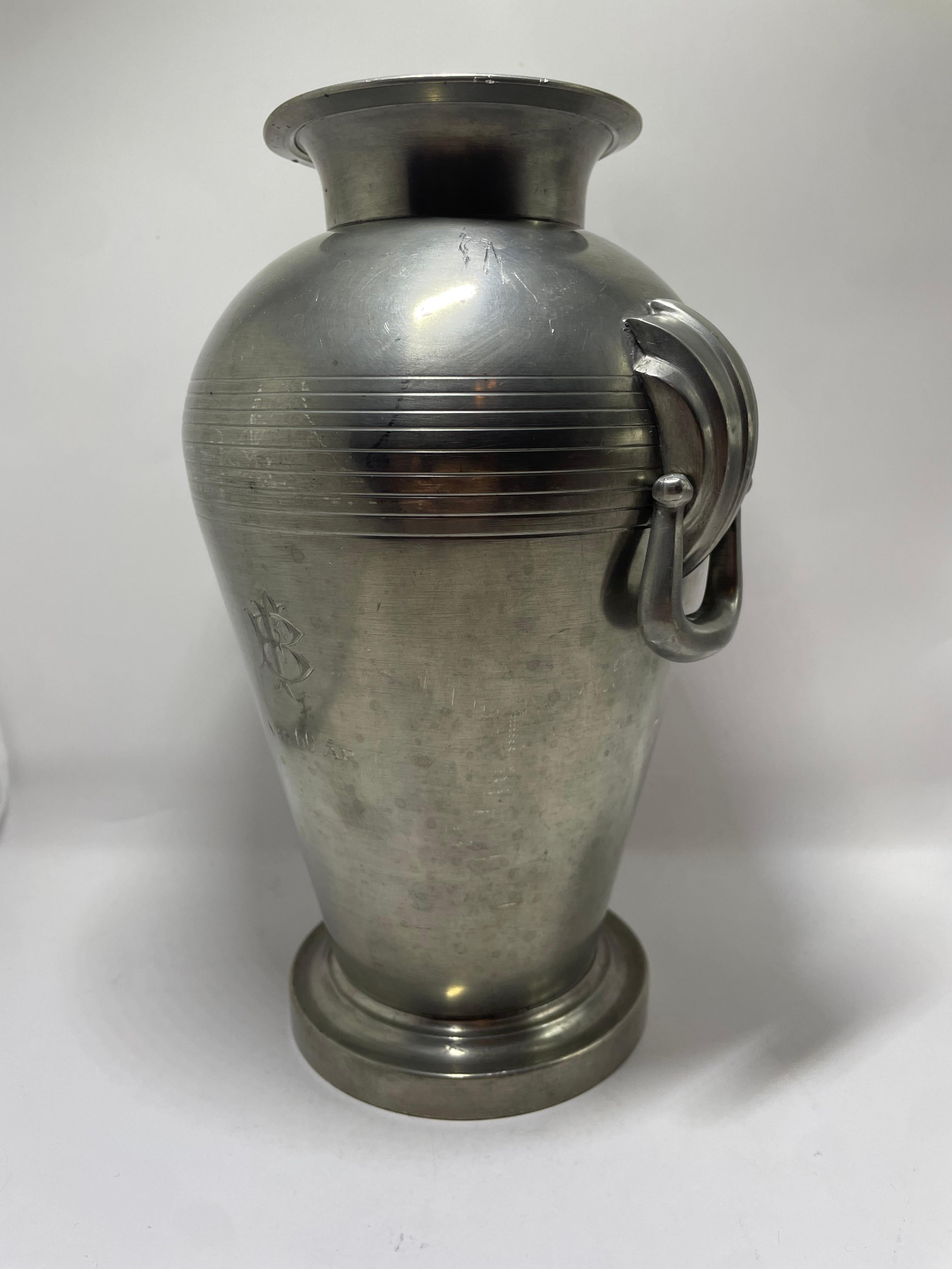 Un bel vaso in peltro progettato e prodotto da Guldsmedsaktiebolaget (GAB) in Svezia, datato 1937. Questo elegante pezzo presenta una forma classica ispirata all'Amphora con bordo sottilmente svasato, una fascia decorativa orizzontale sulla spalla e