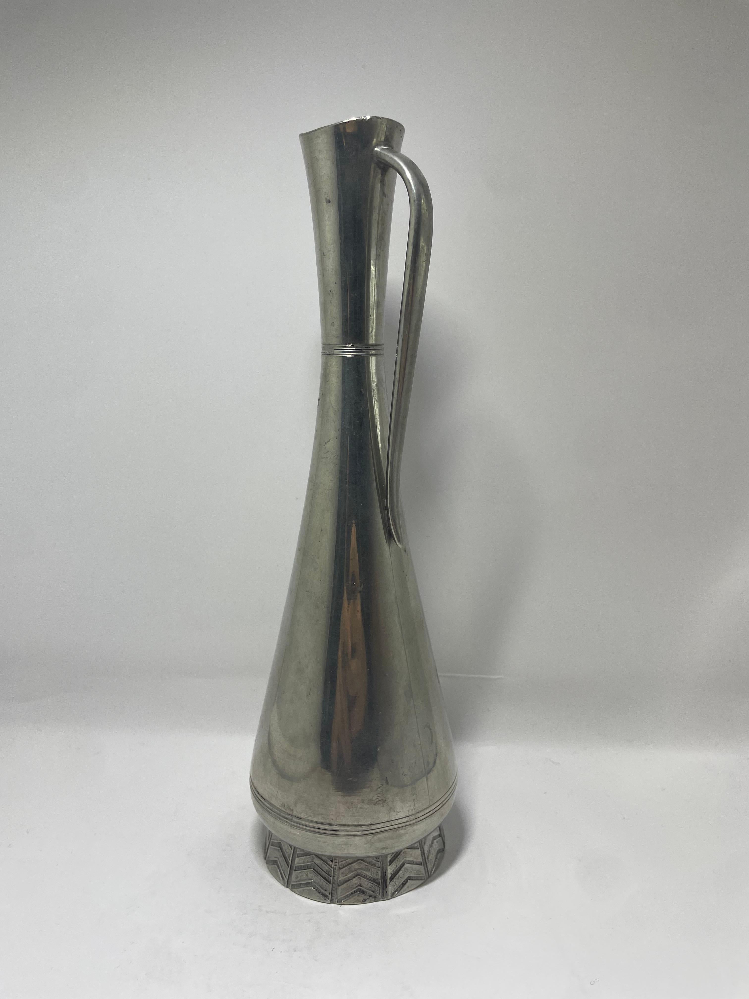 Un sorprendente vaso alto in peltro realizzato da GAB (Guldsmedsaktiebolaget) in Svezia durante gli anni '60. Questo pezzo scultoreo presenta un'elegante forma a goccia allungata con un collo stretto e un manico elegantemente curvo. La base è ornata