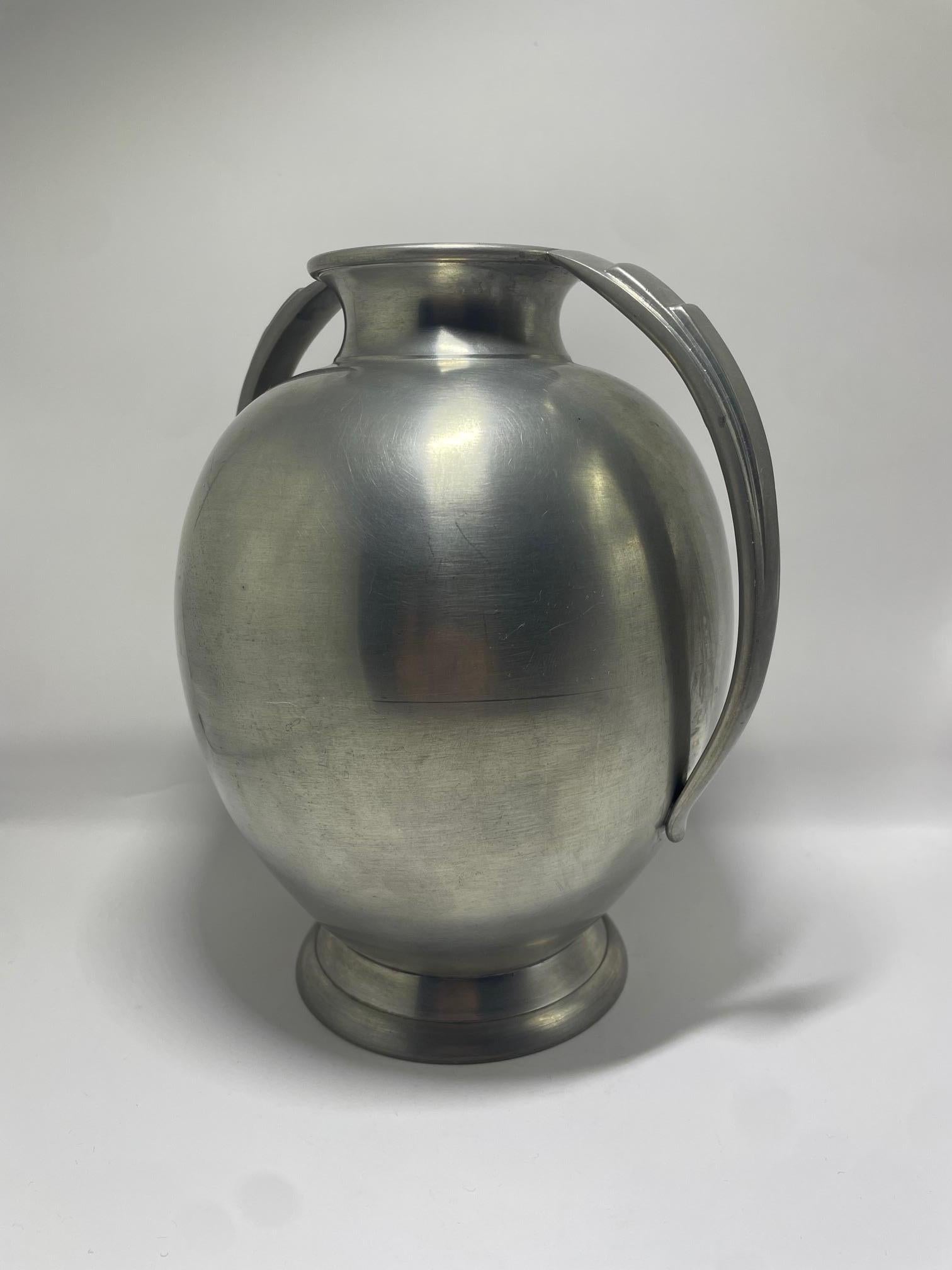 Questo elegante vaso in peltro è stato realizzato nel 1936 da GAB (Guldsmedsaktiebolaget), un importante produttore svedese noto per la lavorazione dei metalli di alta qualità. Il vaso presenta un corpo ovoidale arrotondato con una base svasata e