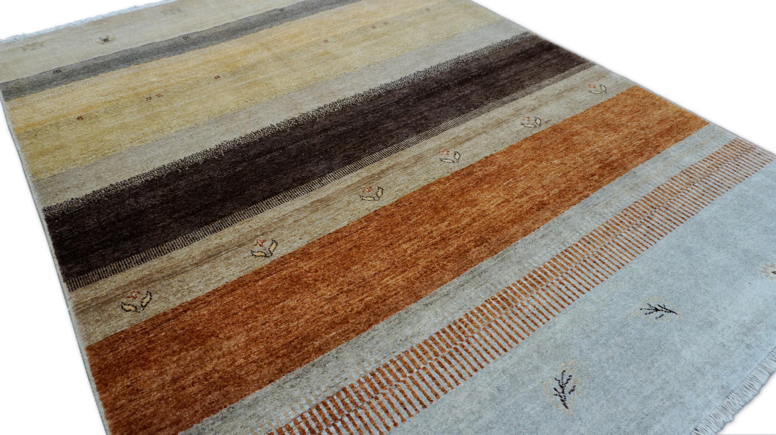 This hand-knotted wool rug draws inspiration from traditional Gabbeh designs, celebrated for their simplicity, natural dyes, and subtle tribal motifs. Featuring a horizontal stripe composition in a serene palette of warm earth tones—ranging from
