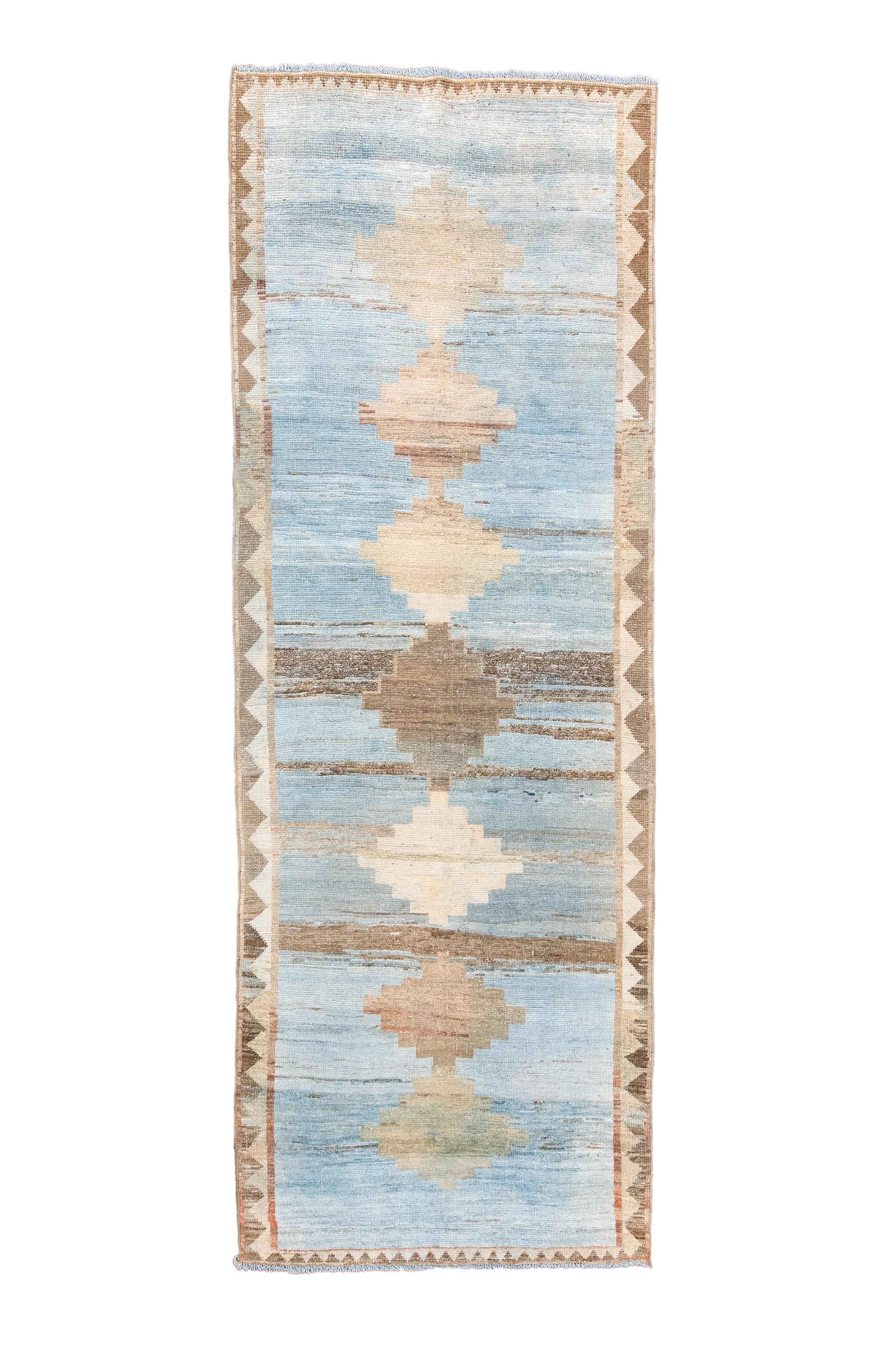 Ce kellegi (long tapis) tribal de Qashqai présente un champ bleu pâle abrasé de façon aléatoire en terre de sienne, avec un pôle central composé de sept diamants étagés. La bordure bitonale est composée de triangles réciproques écru/paille et marron