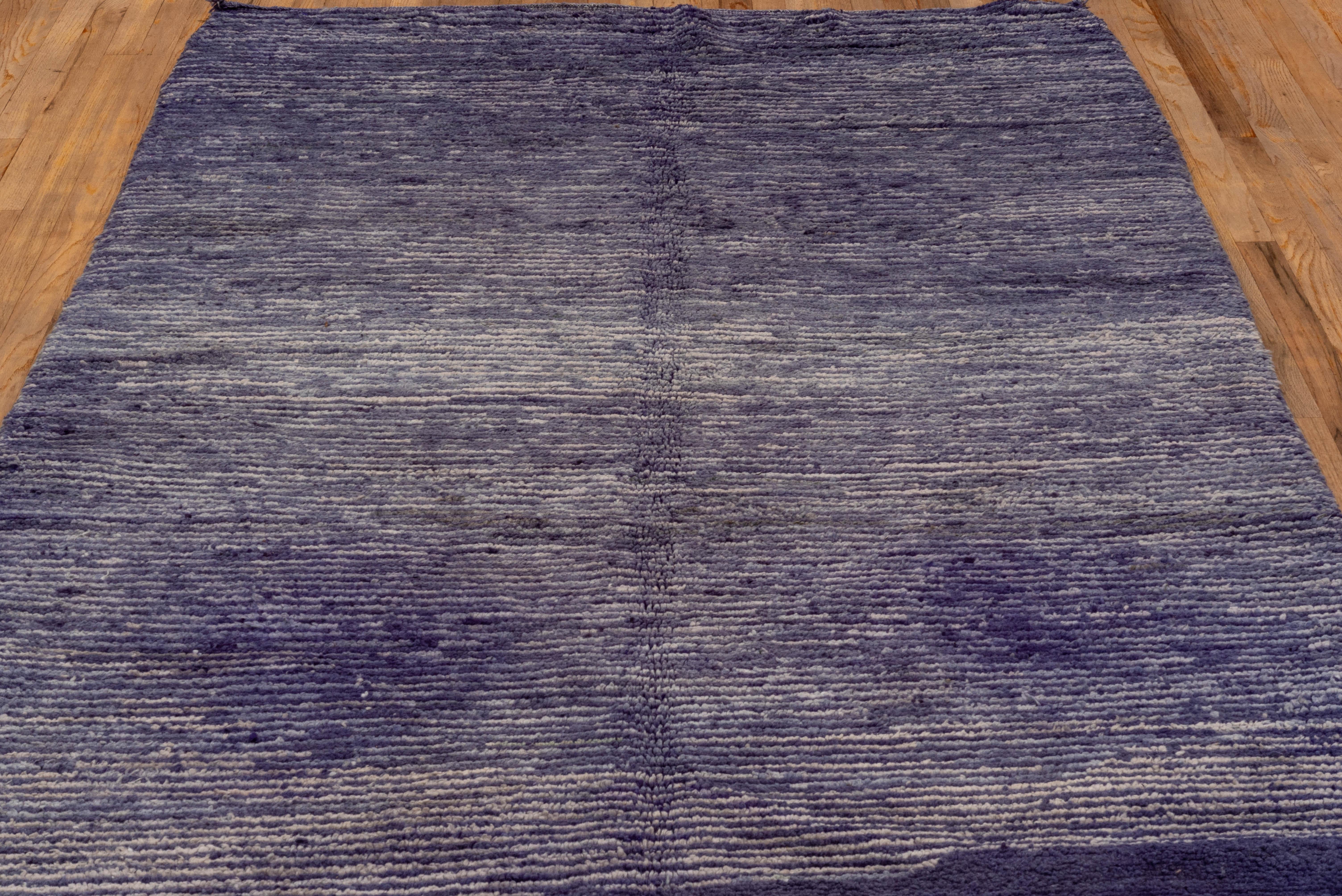 This contemporary hand-knotted Gabbeh rug captivates with its richly saturated indigo gradient and minimalist striated texture. Woven with wool using traditional knotting techniques, the rug presents a nuanced interplay of deep purples, moody