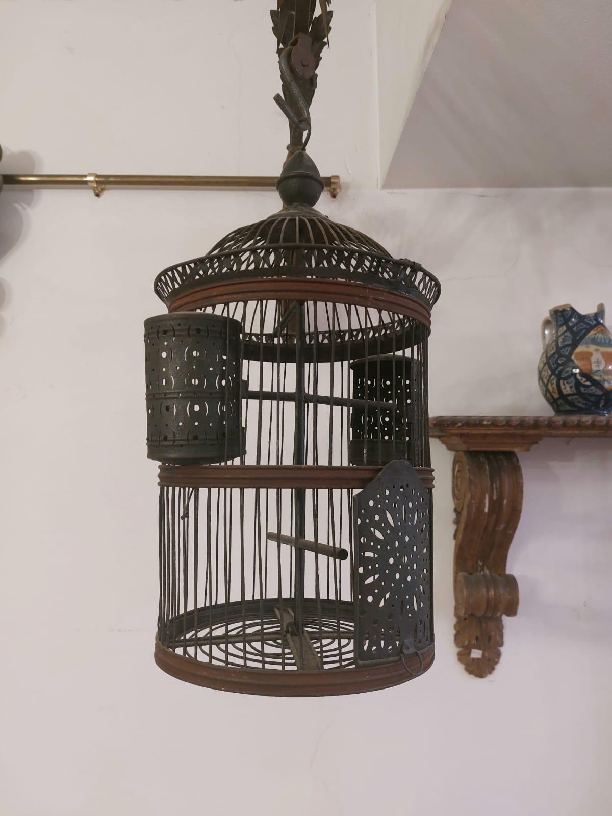 La jaula de hierro y chapa tiene forma cilíndrica, está equipada con una puerta que se desliza hacia arriba y a los lados con dos pequeños comederos (uno para el grano y otro para el agua), con la parte superior en forma de cúpula. En el vértice de