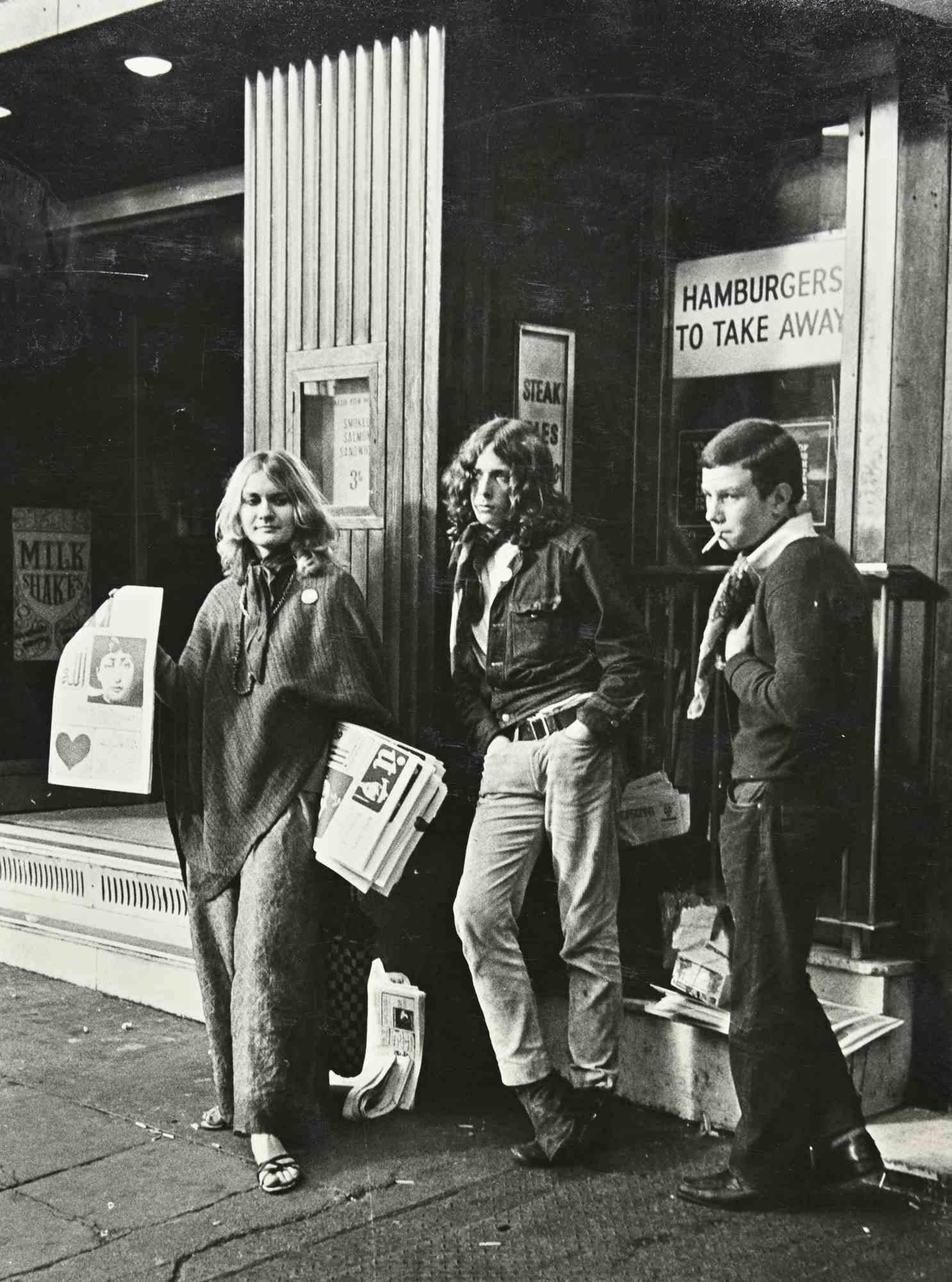 Piccadilly Circus ist ein schwarz-weißes Vintage-Foto, das in den 1970er Jahren von Gabria Belloni realisiert wurde. 

Guter Zustand und gealtert.

Das Foto zeigt junge Straßenverkäufer von verbotenen Zeitungen in London.

Es gehört zu einem