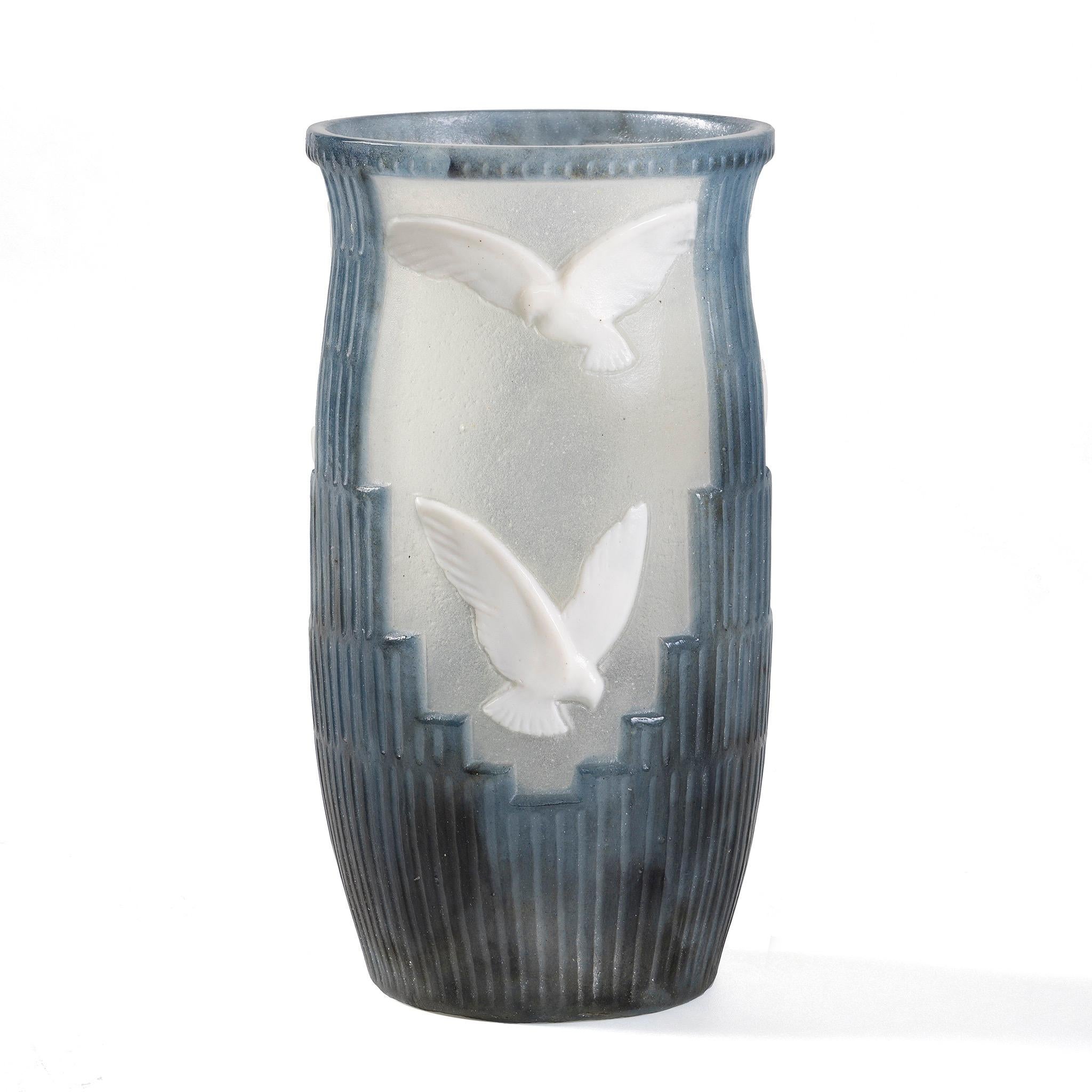 In this modernist Art Deco piece by Argy Rousseau, eight white doves in cameo glass gracefully soar among a skyline of skyscrapers. The buildings are depicted in the iconic setback style, a hallmark of Art Deco architecture where structures recede