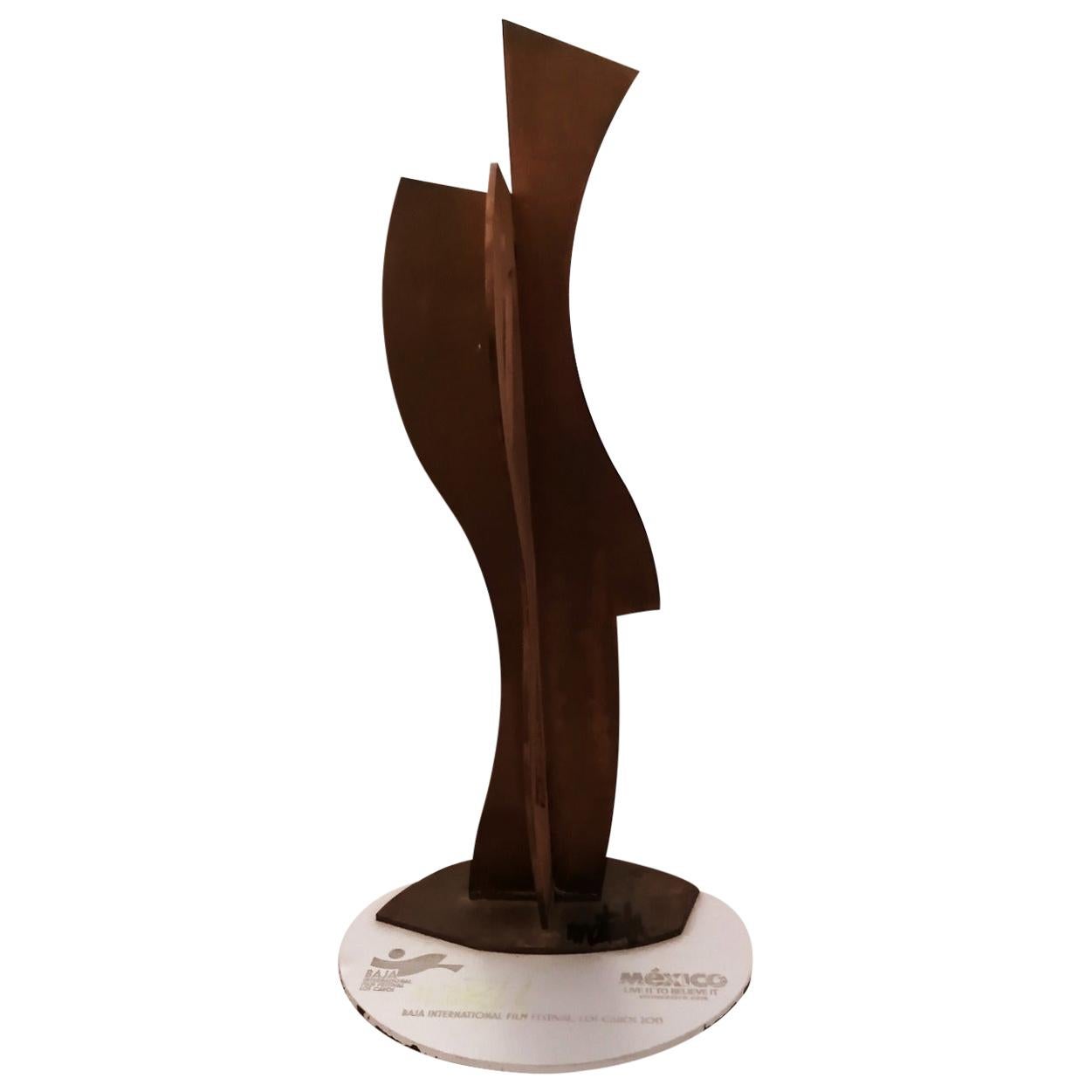 A statuette awarded in the 2013 edition of the Baja International Film Festival in Los Cabos, México. This is a patinated steel sculpture by Mexican artist Gabriel Macotela. The sculpture is signed on the base and the silver plastic plaque under it.