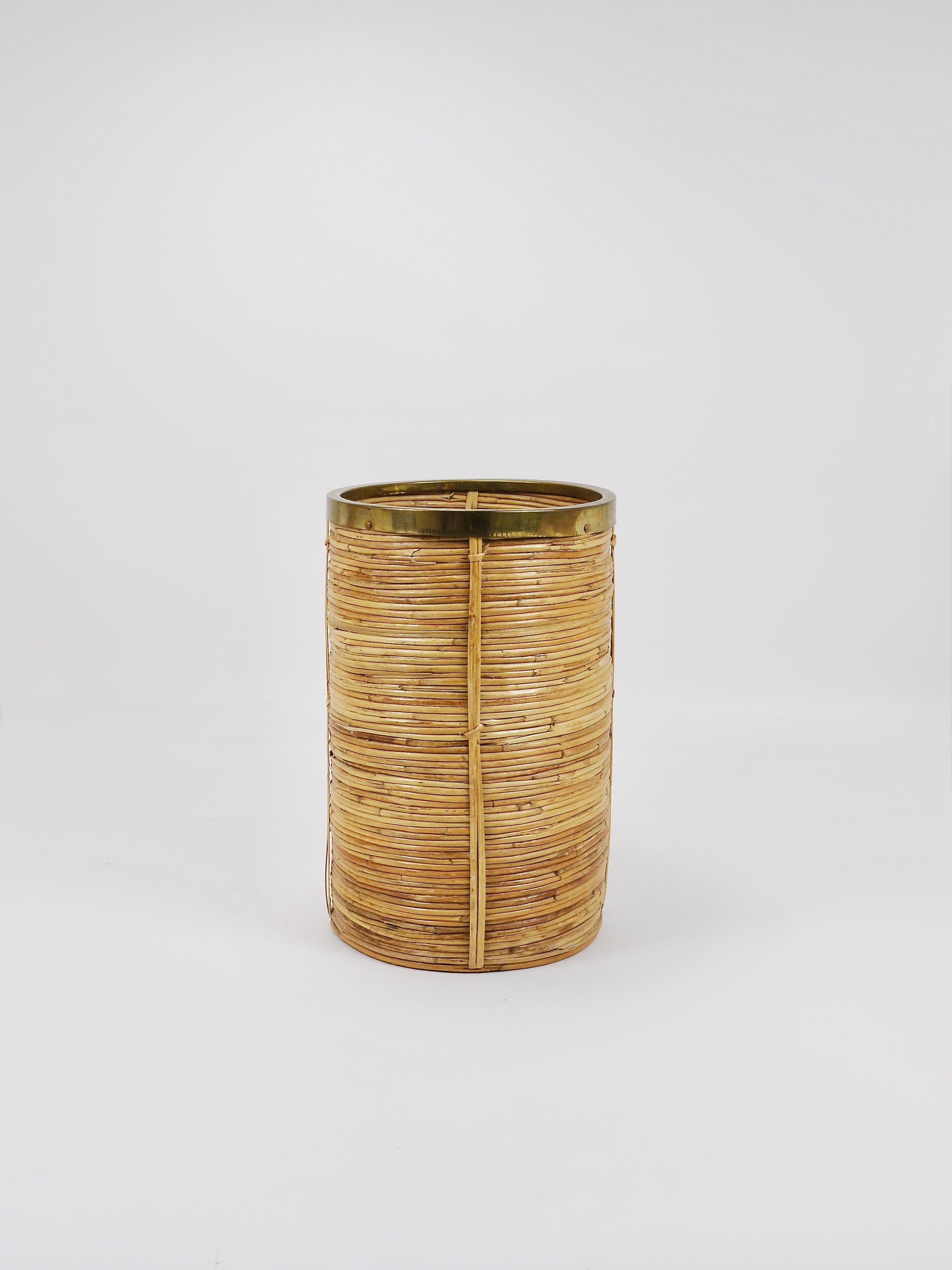 A Mid-Century Modern Hollywood Regency cylindrical umbrella stand / holder, Riviera style wastepaper basket bin from the 1970s. Crafted in Italy. Made from rattan/wicker, complemented by a brass rim atop. Very well preserved, it stands in very good