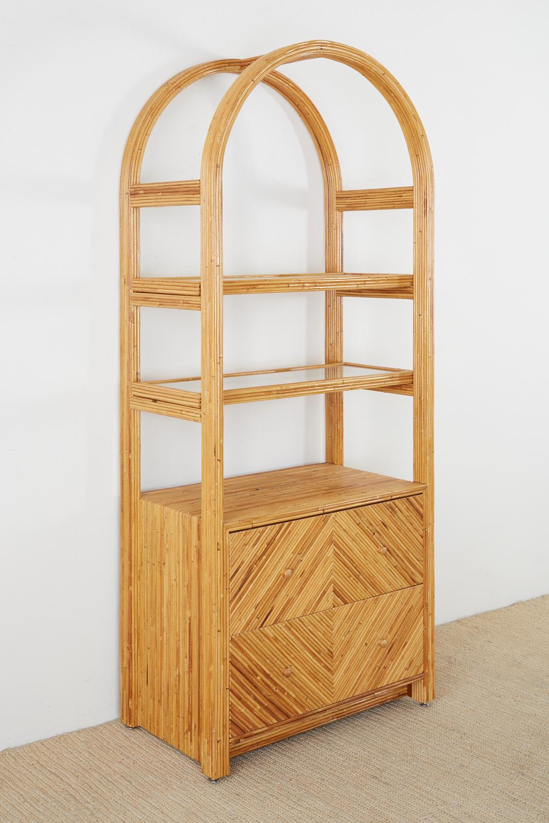 Distinctive Italian étagère display cabinet or bookcase. Beautifully crafted from pencil reeds of bamboo or rattan carefully covering a wood frame. The display features an arched top that holds two open shelves made of cane with a glass top. The