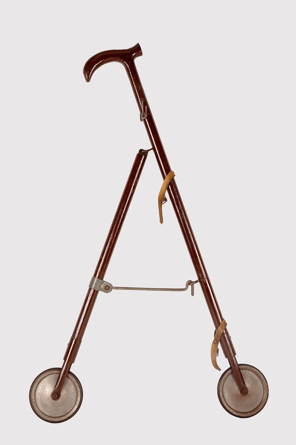 Gadget-System cane: cane with bag holder function. Curious stick used to carry shopping bags, made with two upside-down V-shaped wooden shafts, ending with two small iron and rubber wheels. Under the handle there are two hooks (one on the right and
