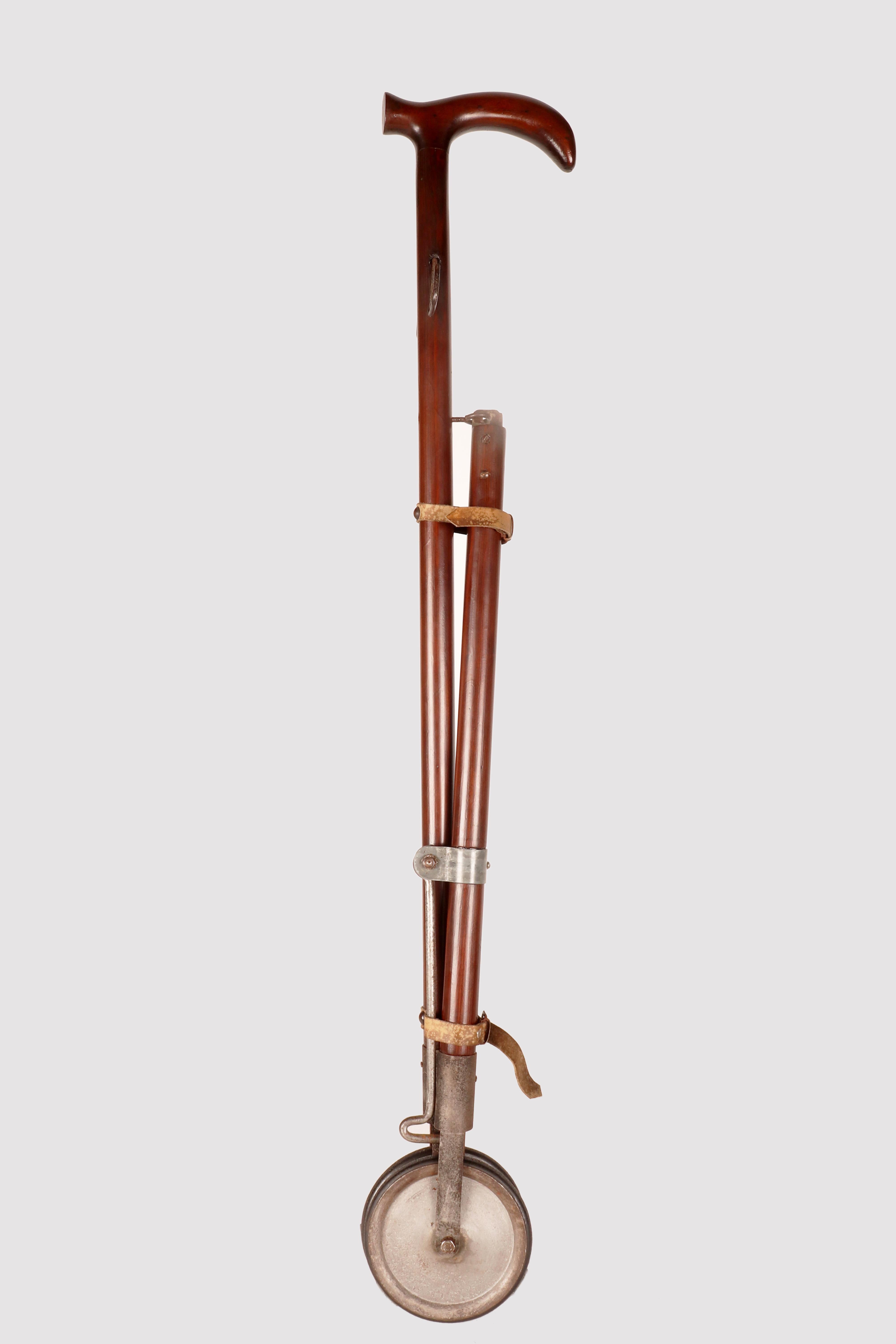 Gadget-System cane: cane with bag holder function. Curious stick used to carry shopping bags, made with two upside-down V-shaped fruitwooden shafts, ending with two small iron and rubber wheels. Under the handle there are two hooks (one on the right