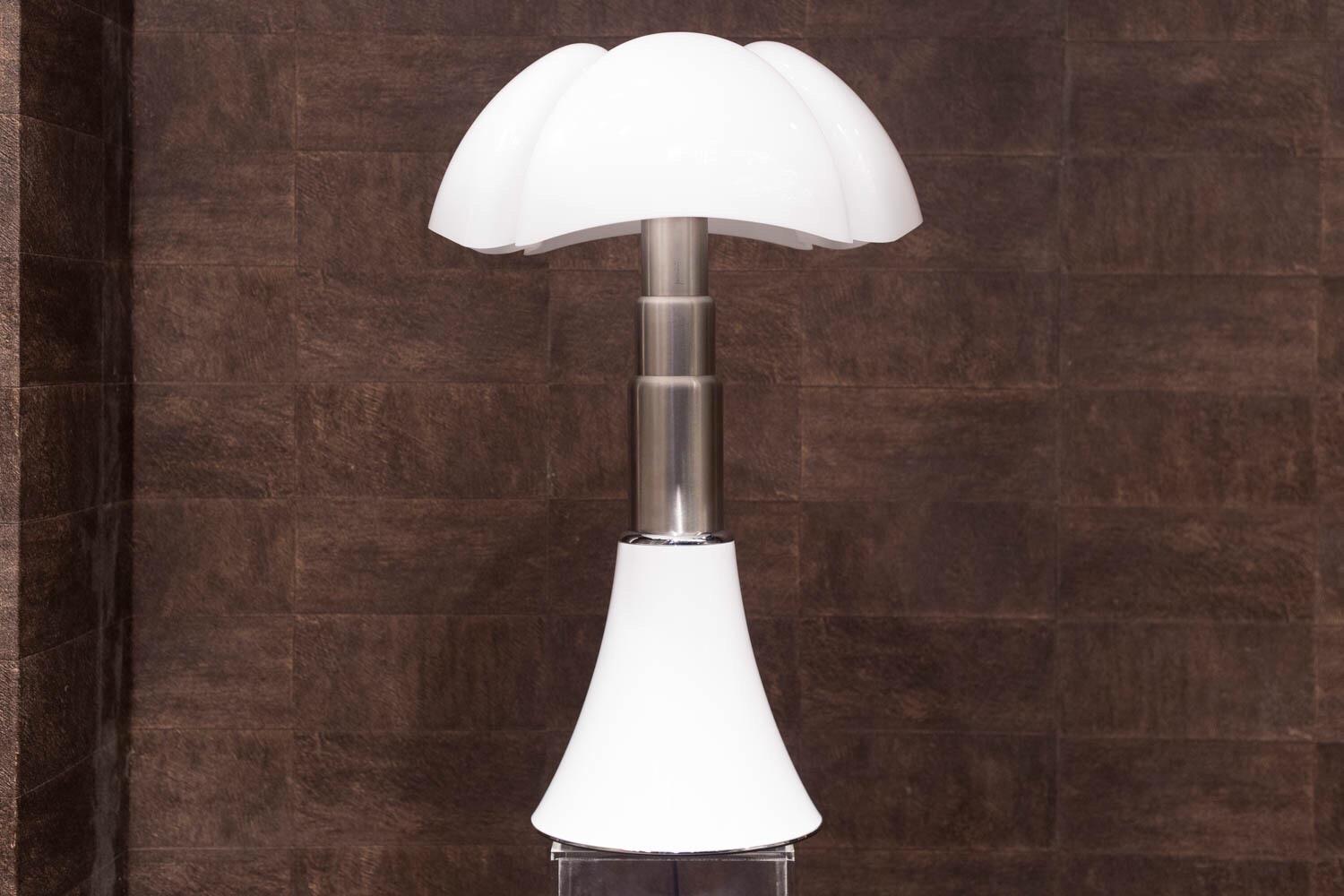 Table lamp or standing lamp with diffused light, adjustable height.
Glazed stainless steel telescope. White opal methacrylate diffuser.
Designed in 1965 by Gae Aulenti for Martinelli Luce. The shape of conic base grows in the height through the