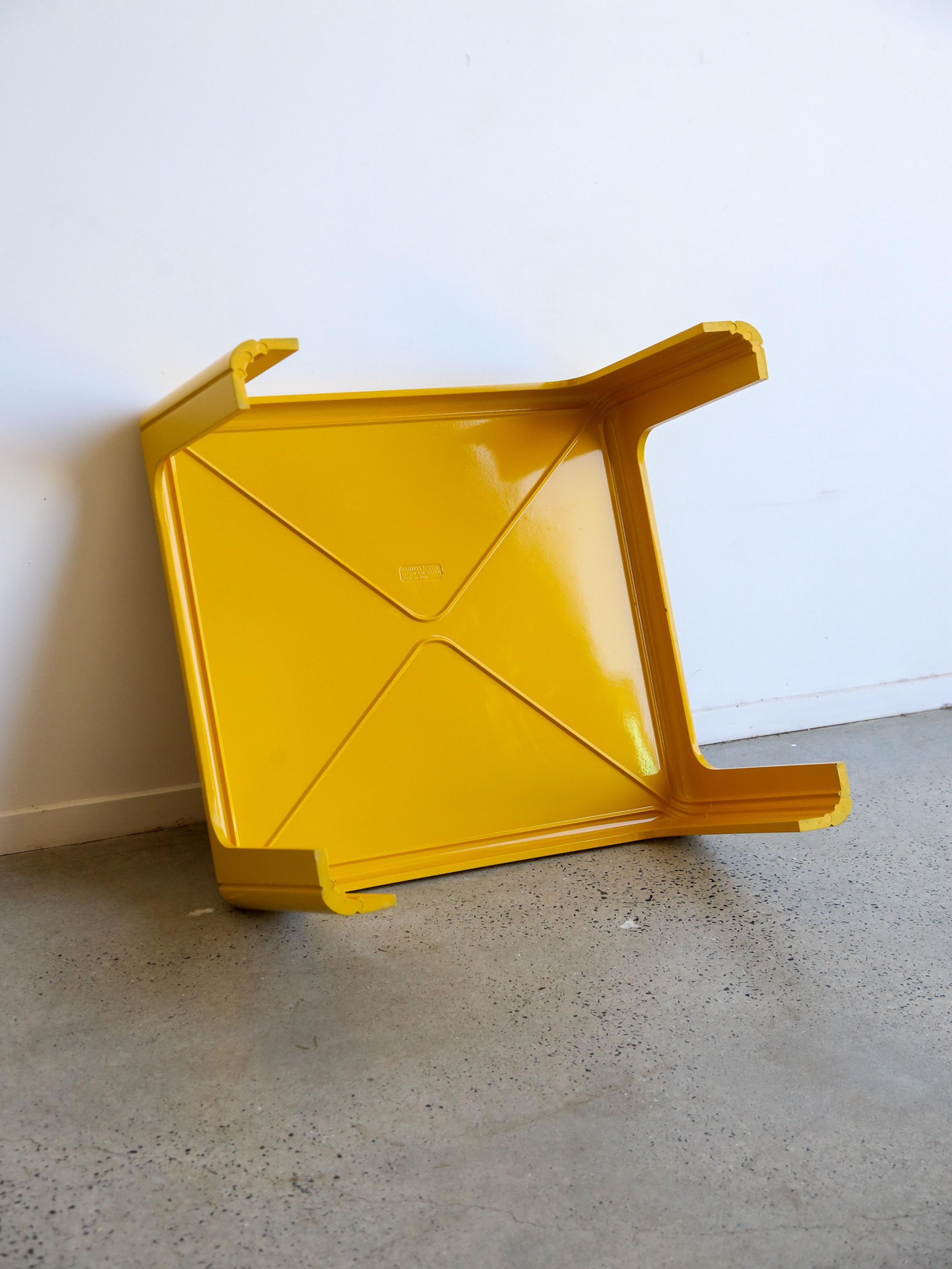 Une table basse carrée aux bords arrondis et lisses, créant une impression de minimalisme et de modernité. Son aspect monolithique est accentué par ses lignes épurées et sa surface uniforme. La finition jaune vibrante ajoute une touche de couleur