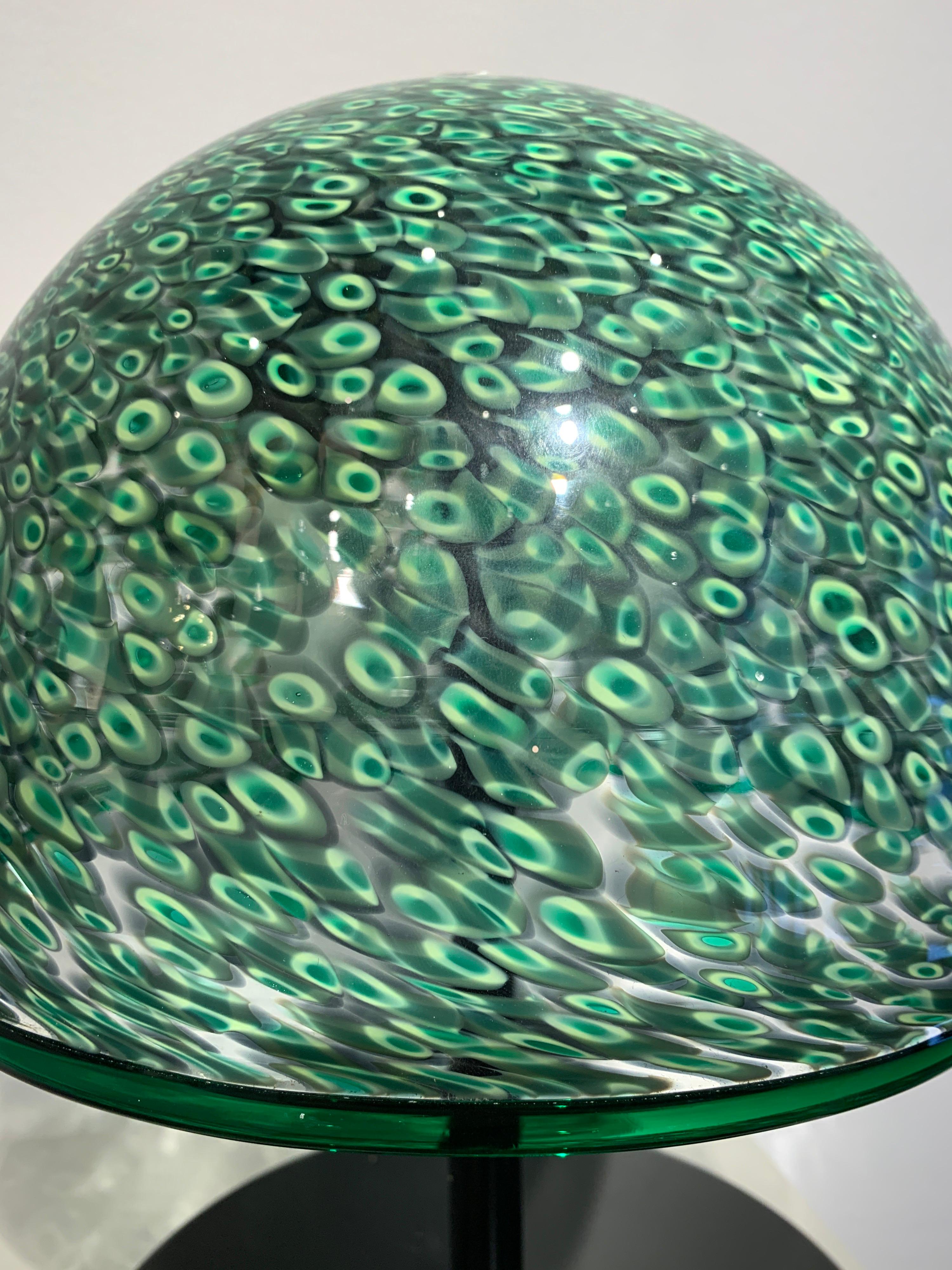 The lamp was designed by Gae Aulenti. The Murrine Glass by Vistosi, famous glass studio in Murano. The mosaic glass, is called Murrine. The lamp is signed Vistosi on the CAP. The foot is black metal.
