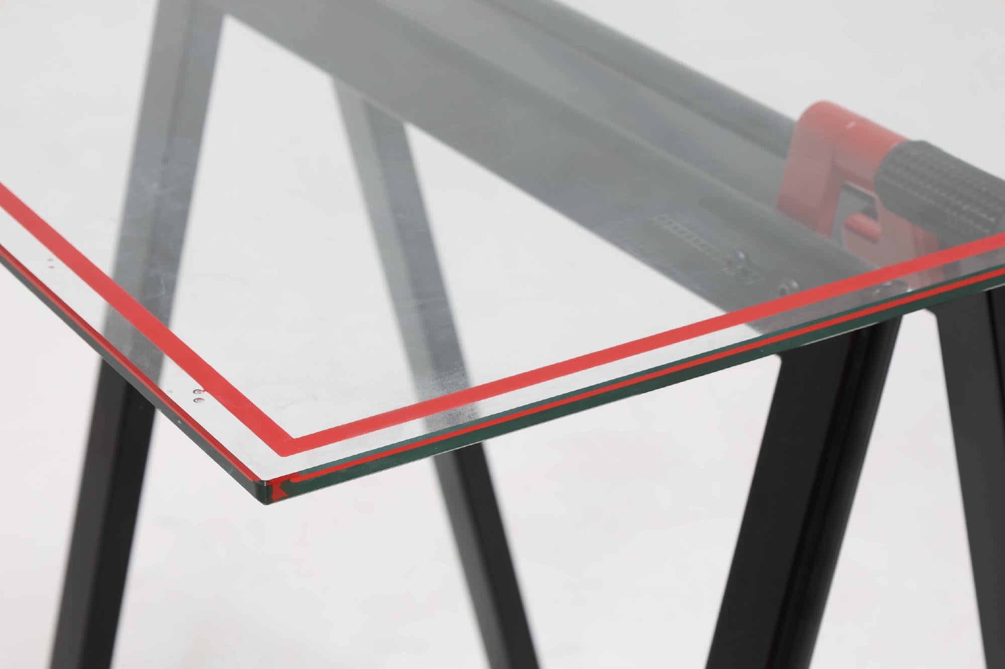 Arbeitstisch / Schreibtisch mit originaler Glasplatte mit zwei schwarz und rot gefärbten, klappbaren Sägeblattbeinen aus Metall. Modell Cardine, Teil der Geatano-Serie, entworfen in den 1970er Jahren von Gae Aulenti für Zanotta, Italien. 

Original