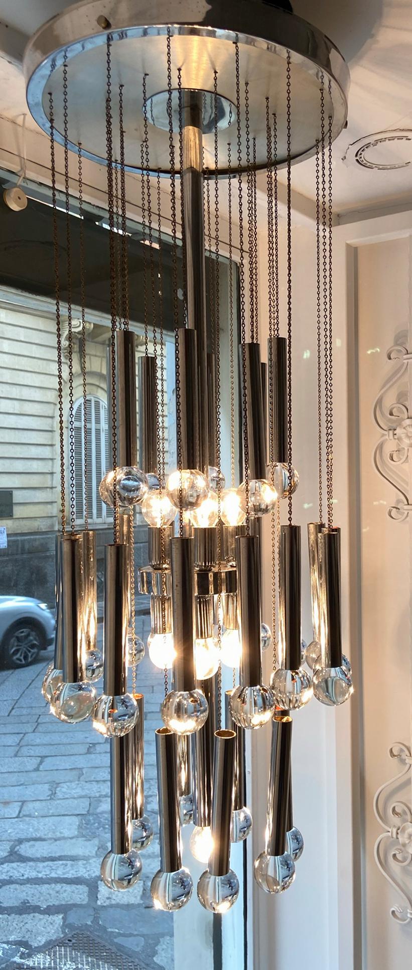 Chrome with chains and glass balls chandelier, circa 1970.
The center stem contains candelabra size sockets and is showed here with clear light bulb, blending in with the glass balls, creating a powerful explosion of reflection on the chrome tube