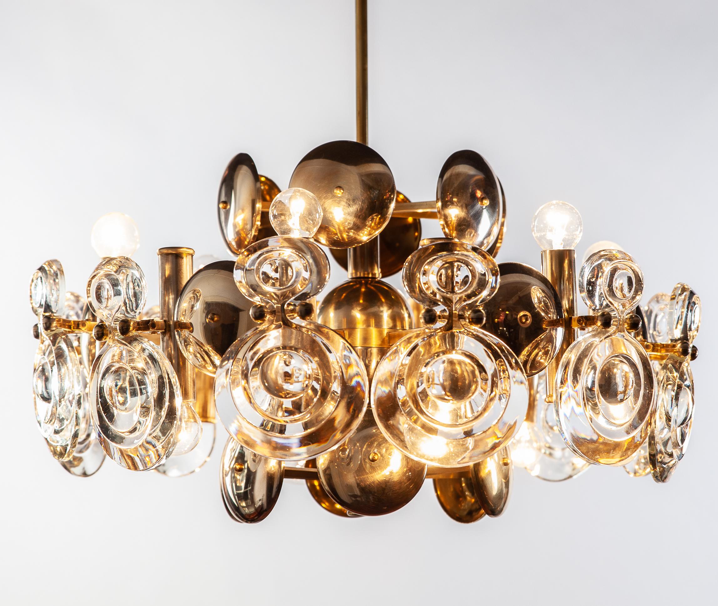 Italian, large midcentury Gaetano Sciolari two-tier chandelier featuring in the original brass finish. Fine optic glass lenses are decoratively and functionally mounted on unusually shaped concave metal shields to serve as reflectors. Top tier holds