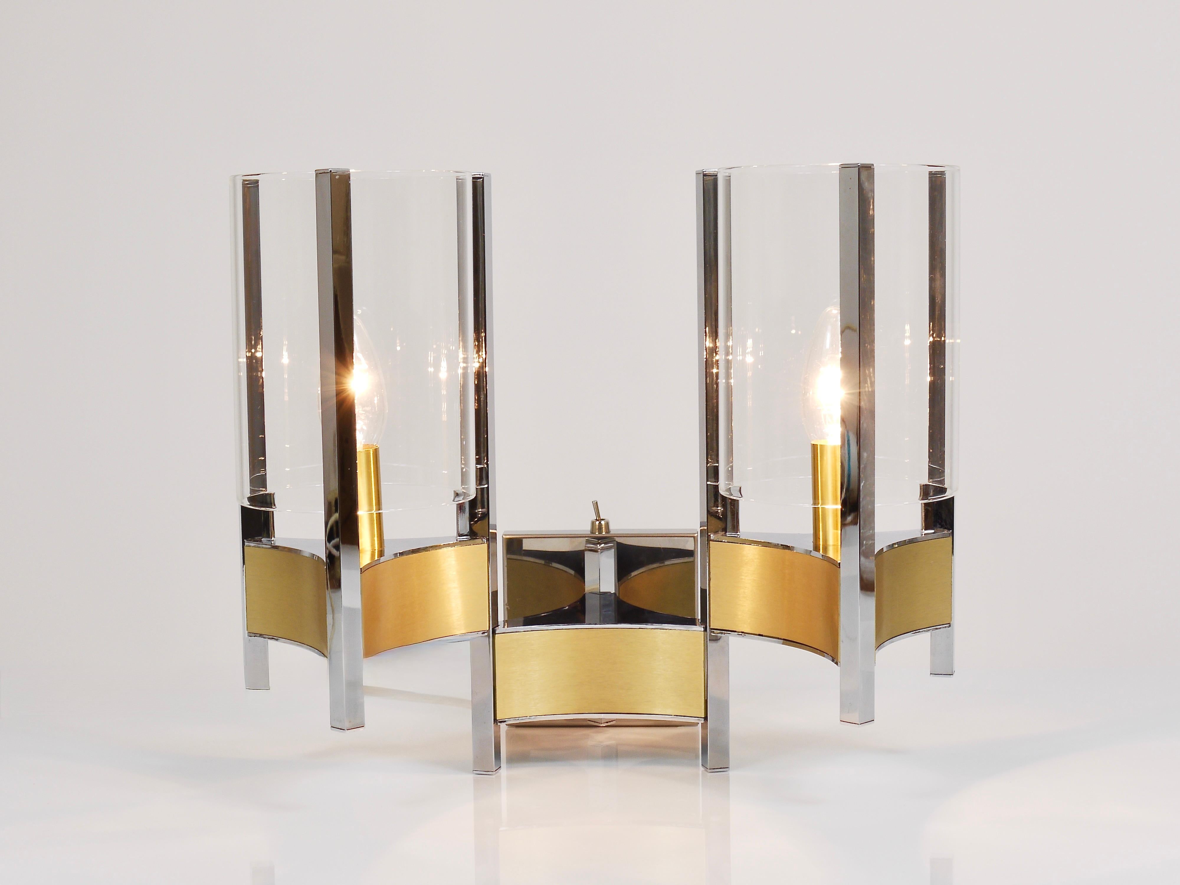 A stunning pair of sculptural wall lamps / sconces from the 1970s, designed and manufactured by Gaetano Sciolari, Italy. Executed in chrome-plated metal and brushed brass, each sconce features two elegant cylindrical clear glass shades. Both pieces