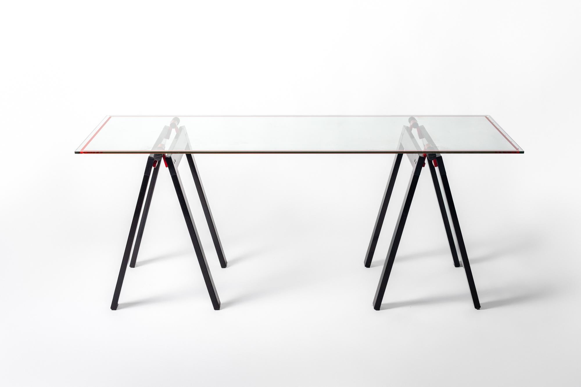 The Gaetano table by Gae Aulenti for Zanotta features its original glass top with black and red enameled metal folding sawhorse legs. 

Gae Aulenti was a renowned Italian architect and furniture designer known for iconic designs including the Jumbo