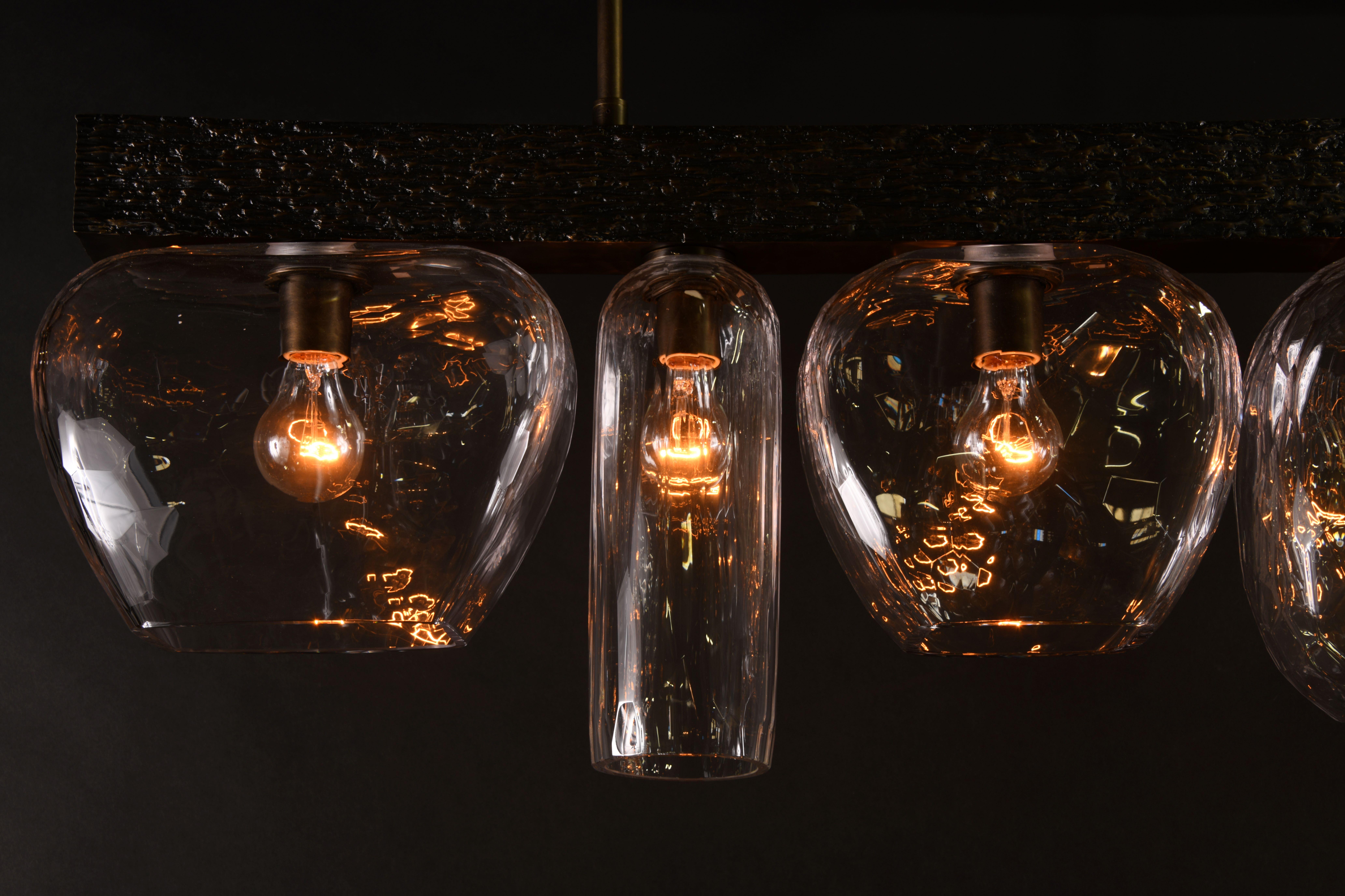 Cluster of heavily pebbled, ribbed glass lanterns suspended from solid bronze frames with cast rough-hewn detailing.

Models in the collection are individually hand-crafted by the skilled artisans in our studio. Custom versions tailored to a
