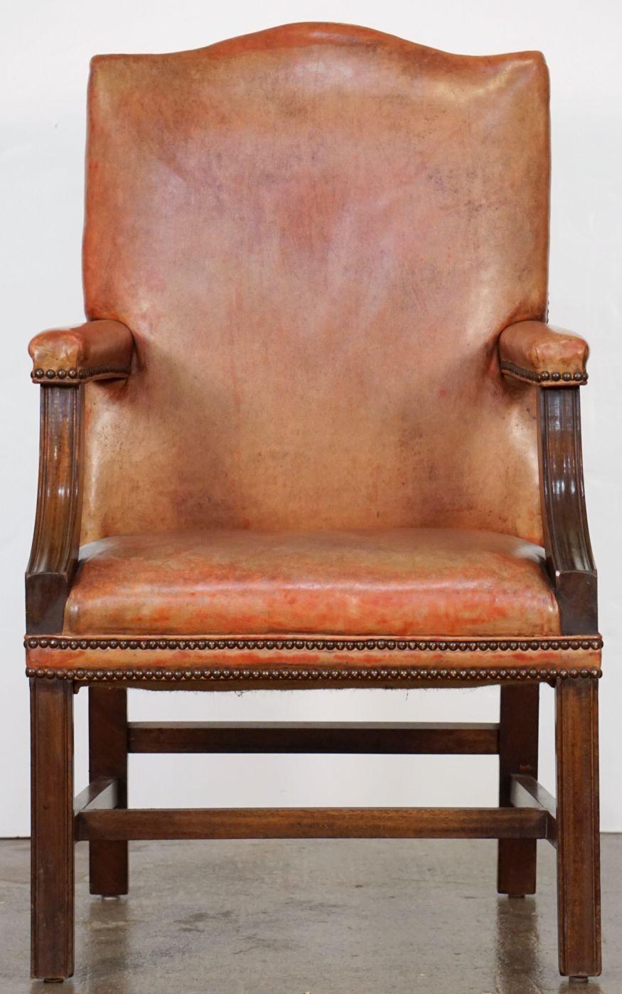 A fine English leather and mahogany Gainsborough armchair - featuring a high back, open sides and shaped arms, with wide comfortable seat, on a mahogany stretcher.
The leather upholstery with brass nail-head trim around the borders.


