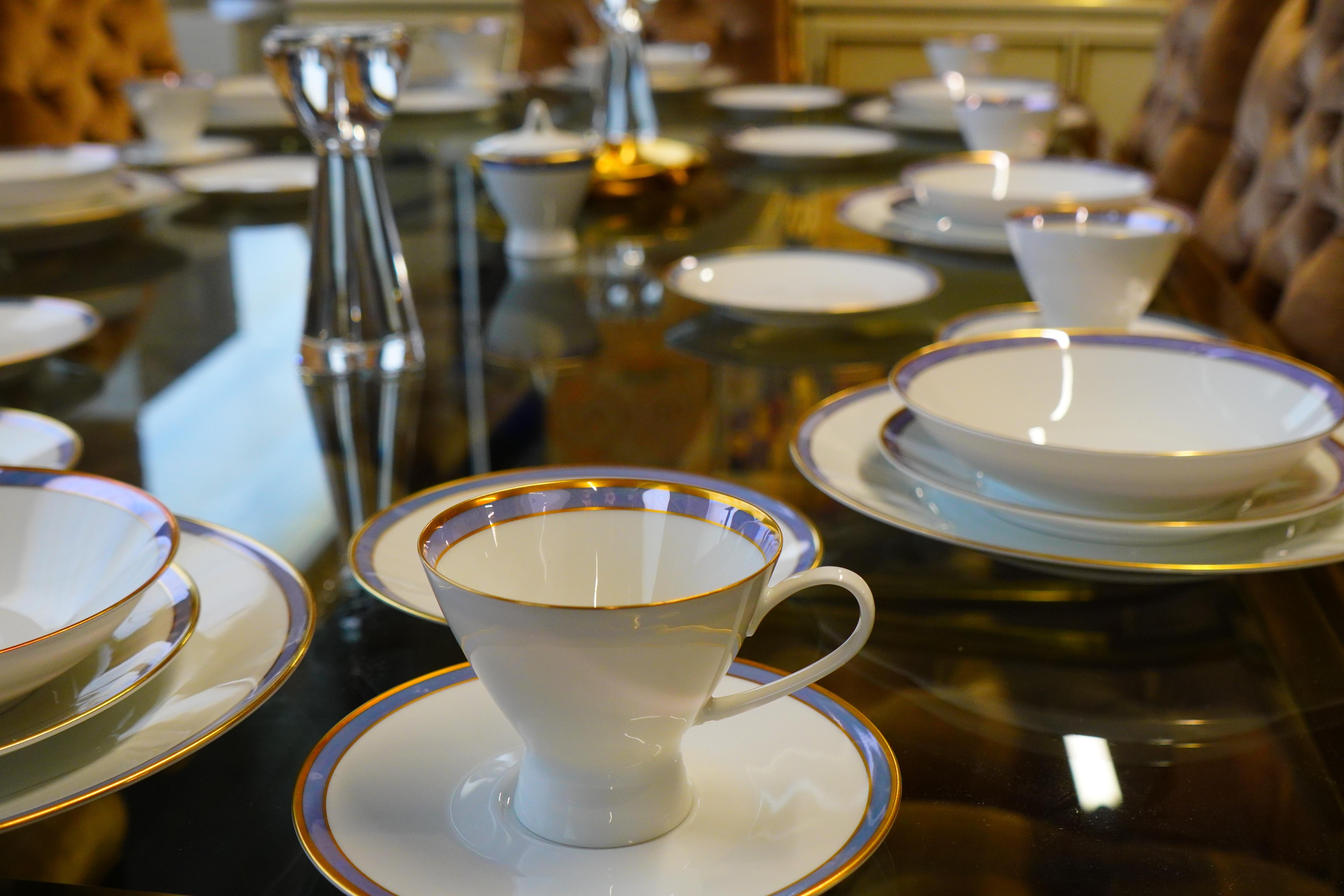 Hübsches Tafelservice aus der Jahrhundertmitte, entworfen von Raymond Loewy für Rosenthal (Deutschland).  Feines Porzellan mit einem schönen irrlichternden blauen Band, das von goldenen (vergoldeten) Bändern umrandet ist.  Dieses 63-teilige Set
