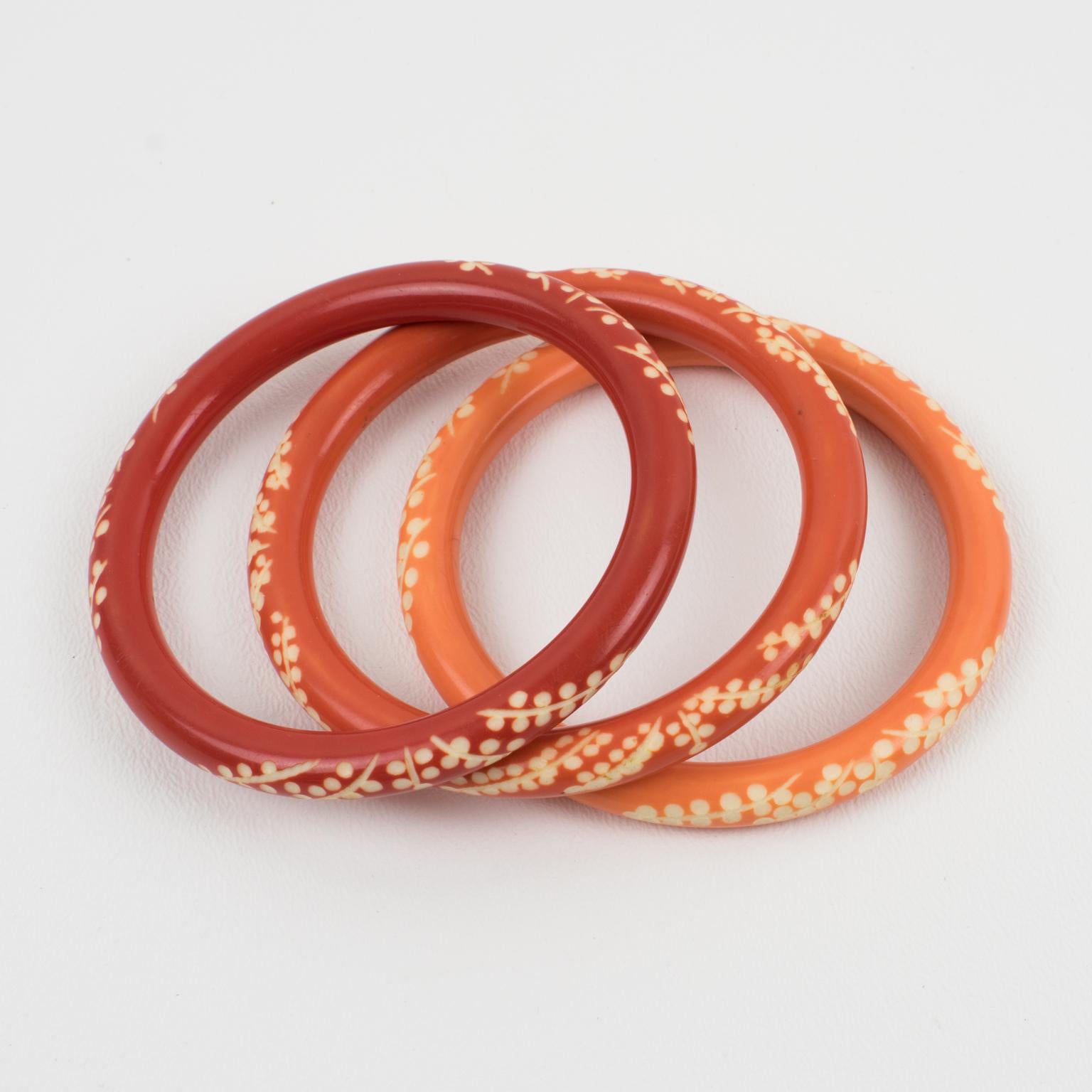 This lovely Galalith bracelet bangle set of three pieces features a chunky spacer domed shape with deep floral carving. The set boasts a trio of orange variations with peach pink, ginger orange, and orange-red spice colors over a white background.