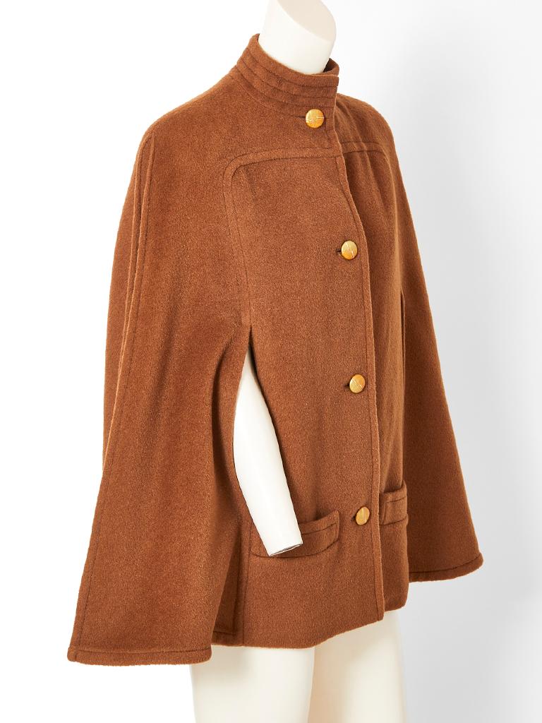 James Galanos, camel hair and vicuña wool cape, having a swing like back, Mandarin, high collar, lower front pockets and leather button closures that are gold leafed.Cape ends just above the thigh. 
Designer : 



